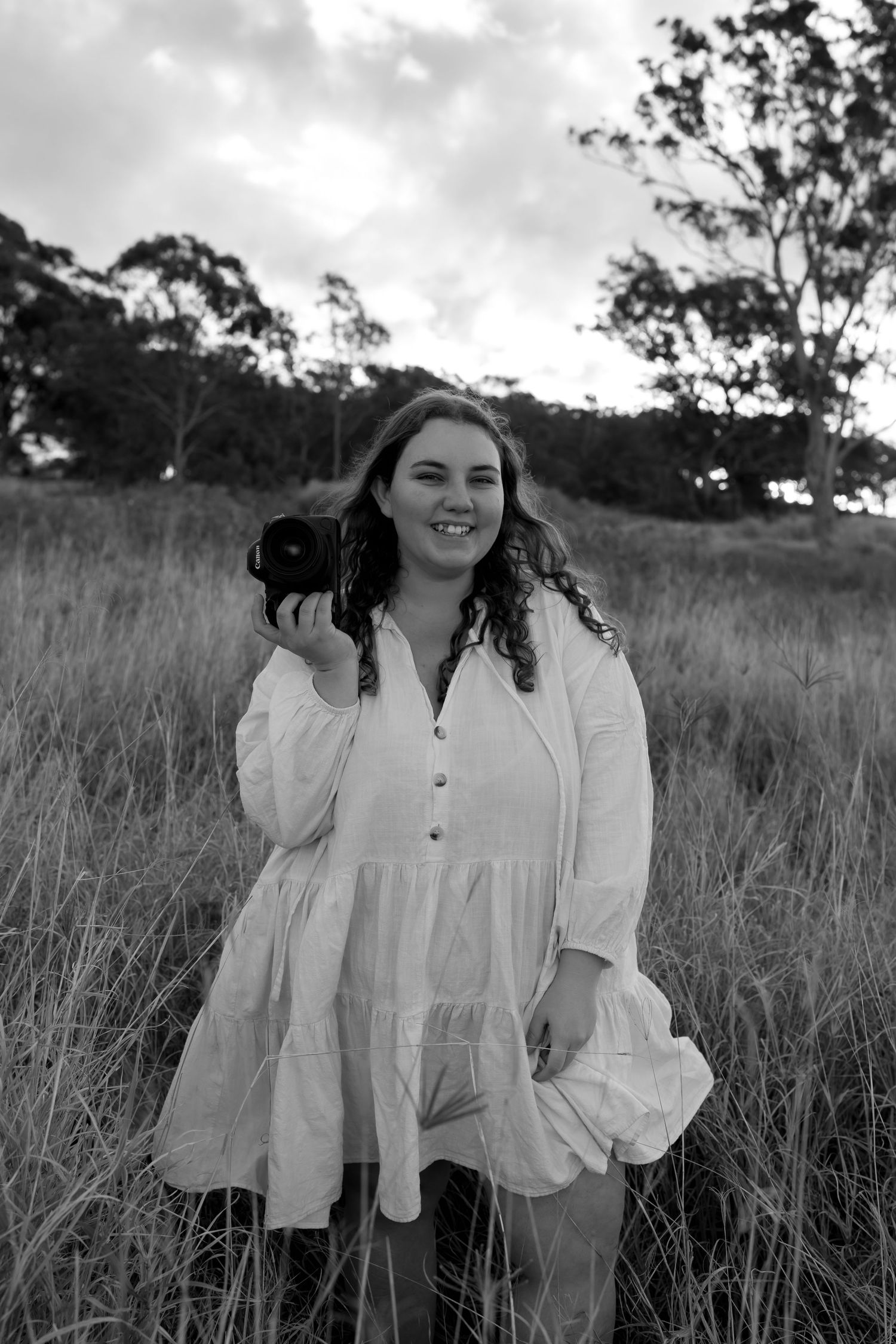 Person in white dress holding camera in golden field during sunset.