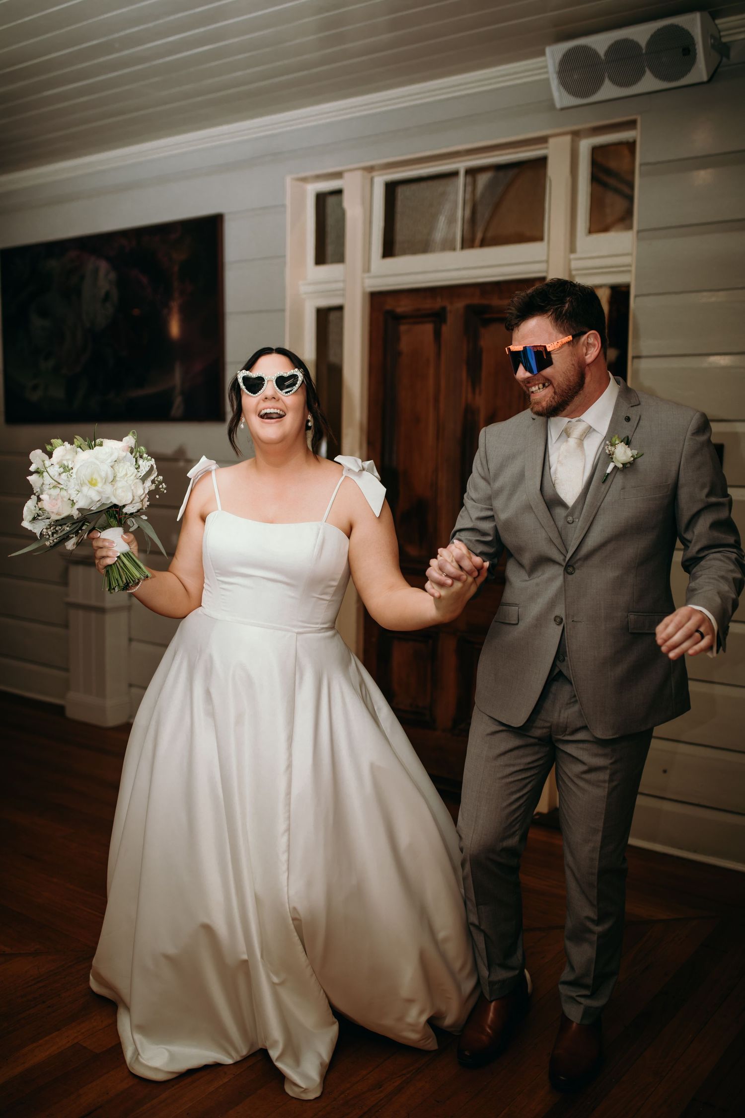 A couple wearing sunglasses and wedding attire pose playfully in a series of candid shots outside a white building.