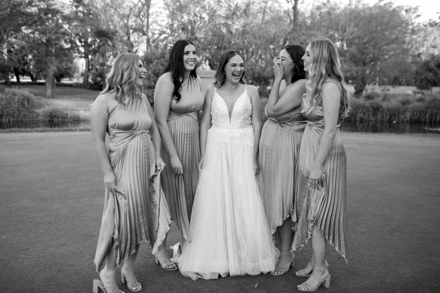 Bridesmaids in striped dresses gather around bride in white gown during outdoor celebration.