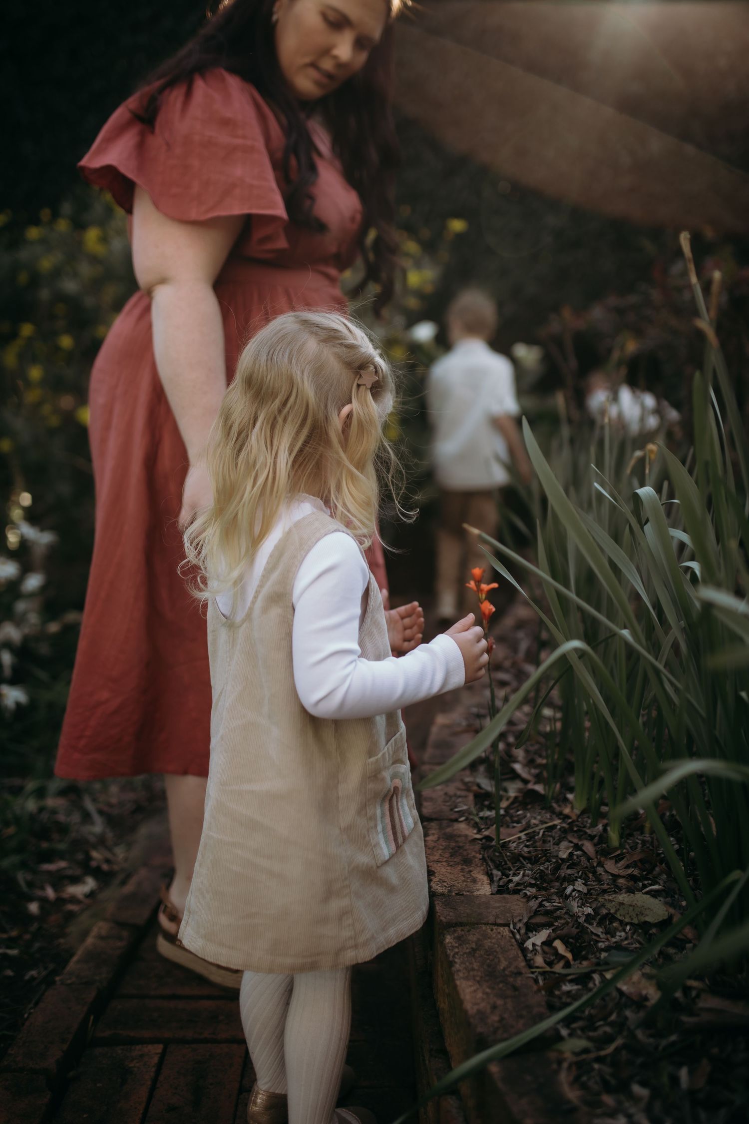 Child exploring garden path wearing beige dress in evening light.