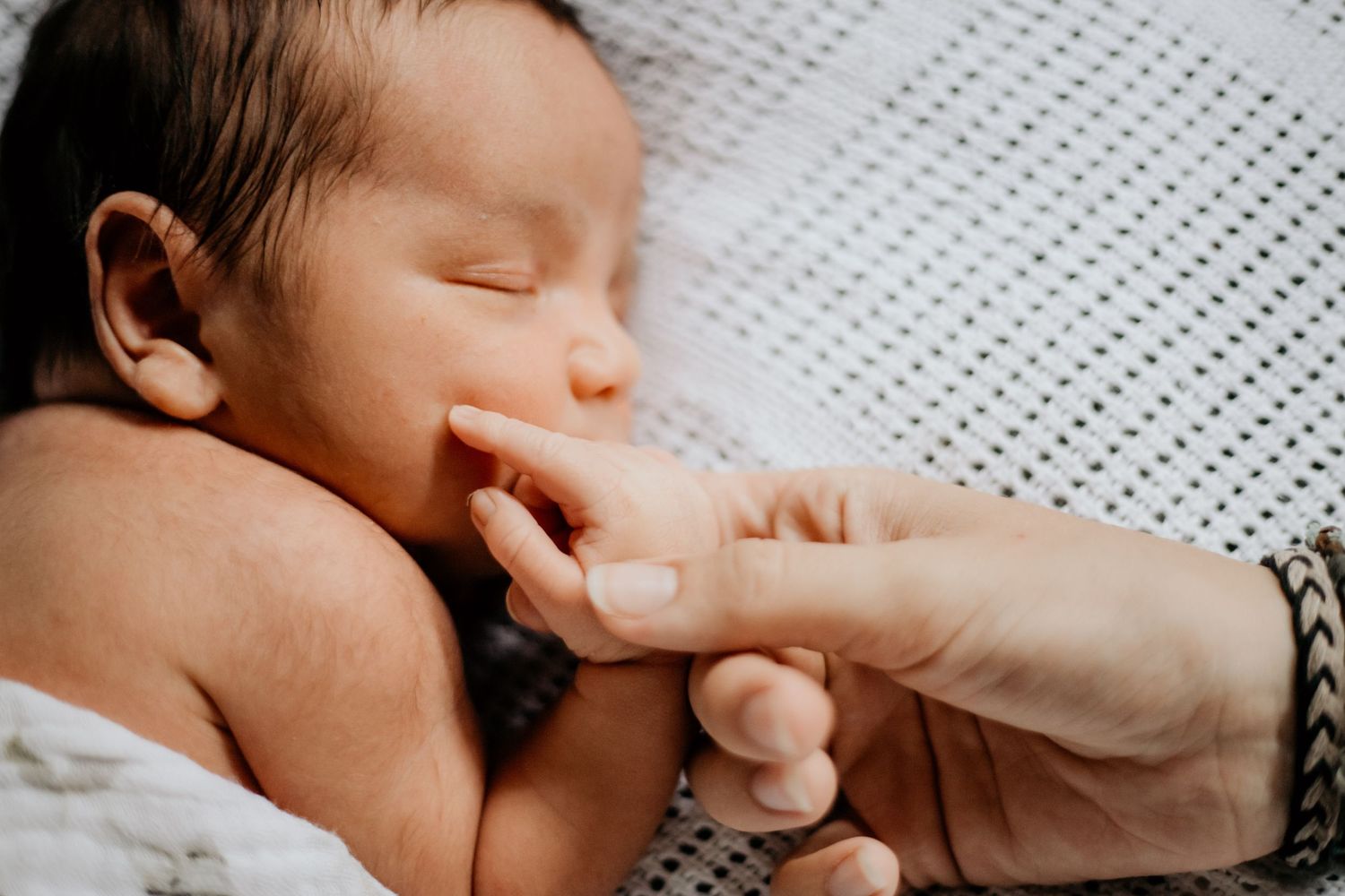 Close-up of tiny newborn hand being held against textured blanket.