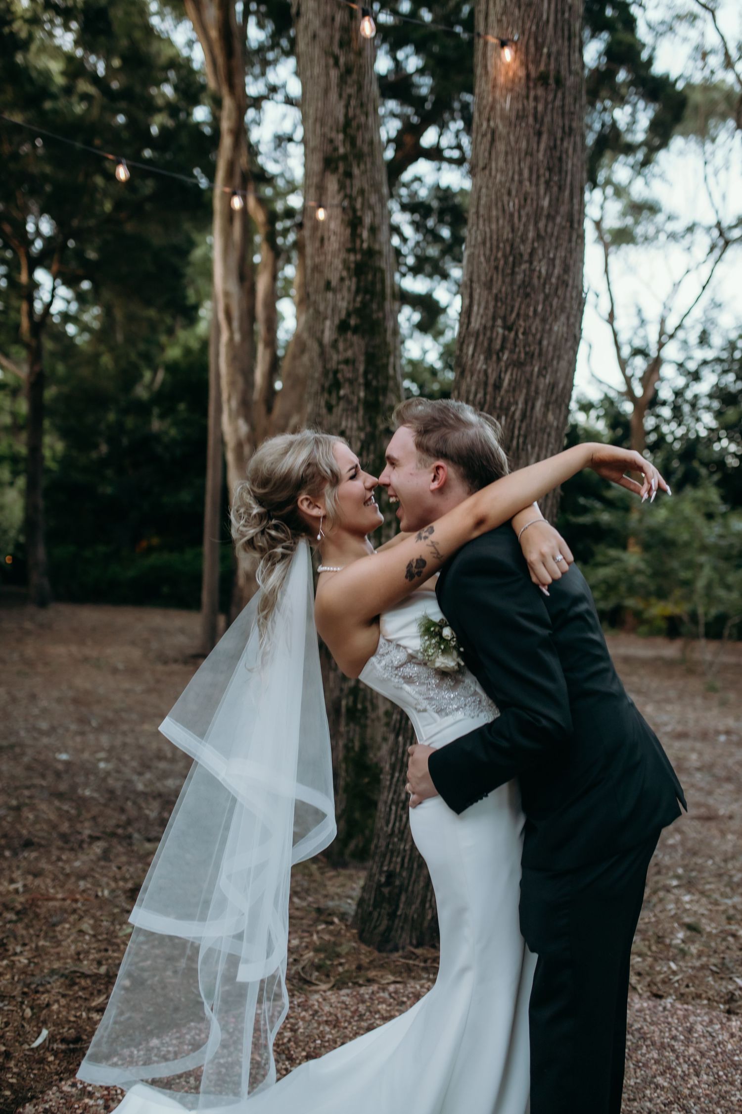 A romantic wedding couple shares intimate moments in a wooded outdoor setting.