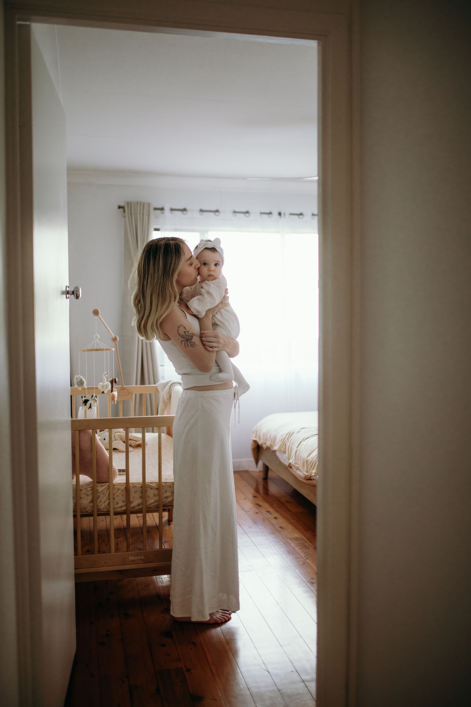 Parent holding infant in nursery room with wooden crib and natural lighting.