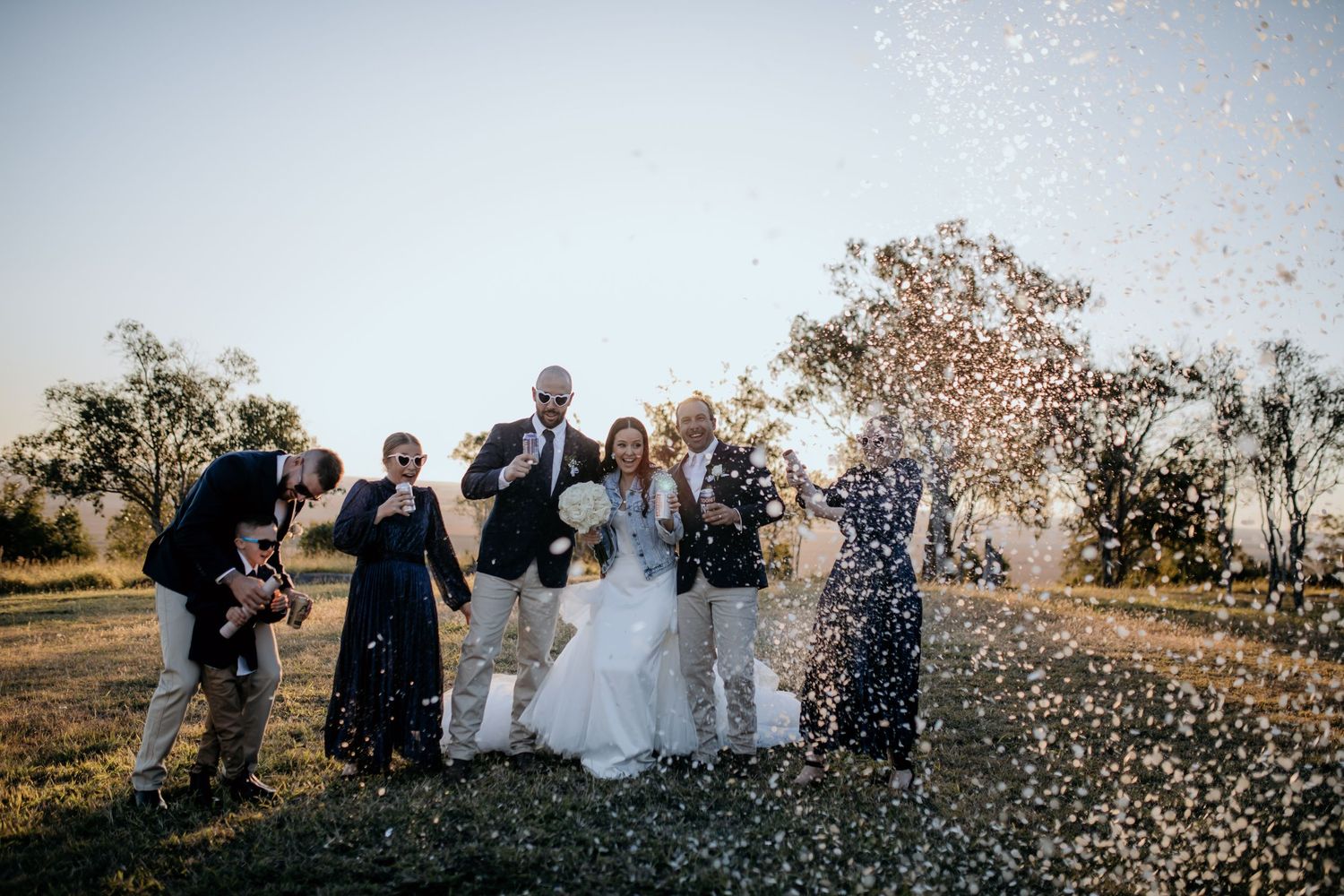 Wedding party celebrates with confetti in a joyous outdoor group shot.