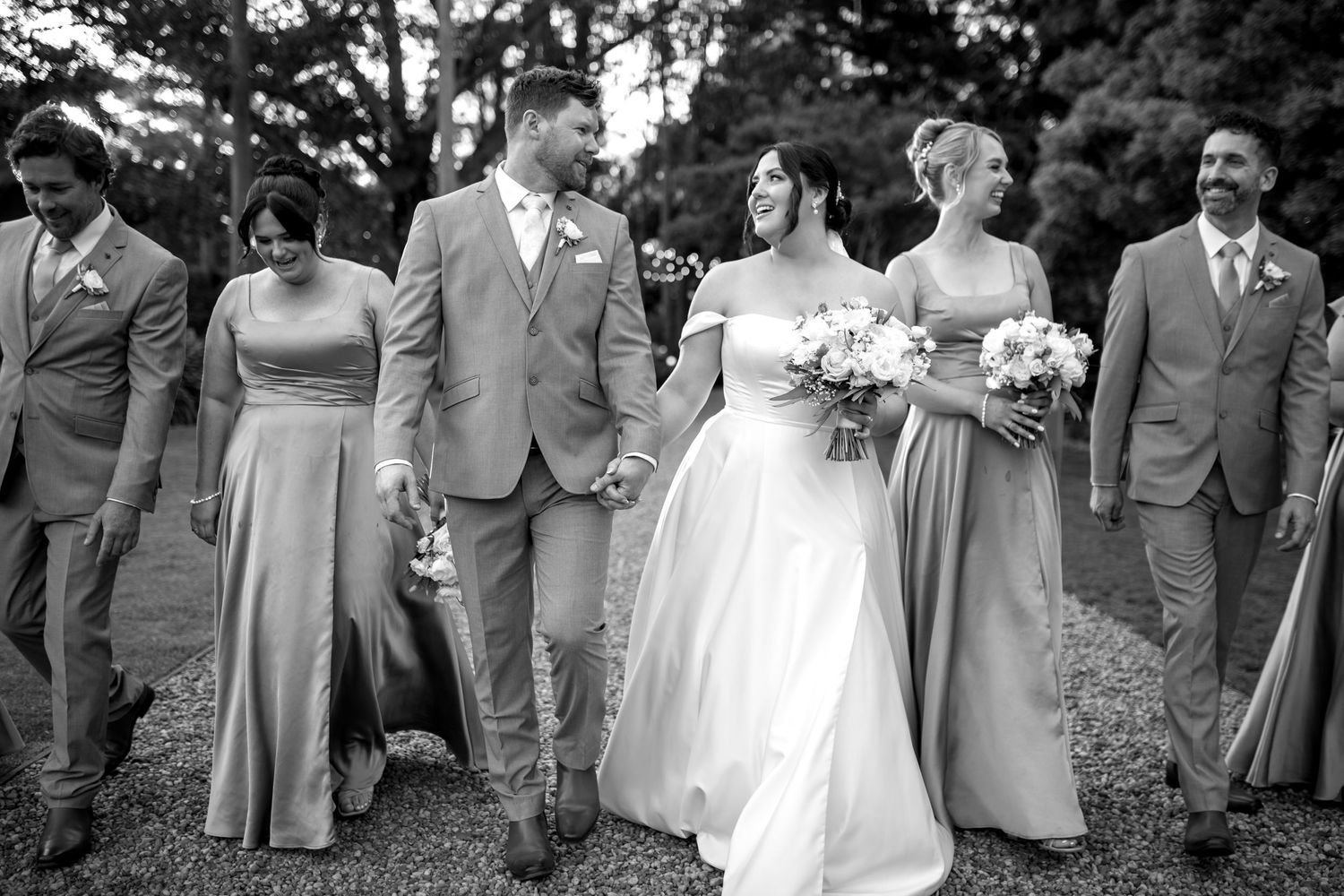 A wedding party lineup in coordinated grey suits and dresses poses outdoors.