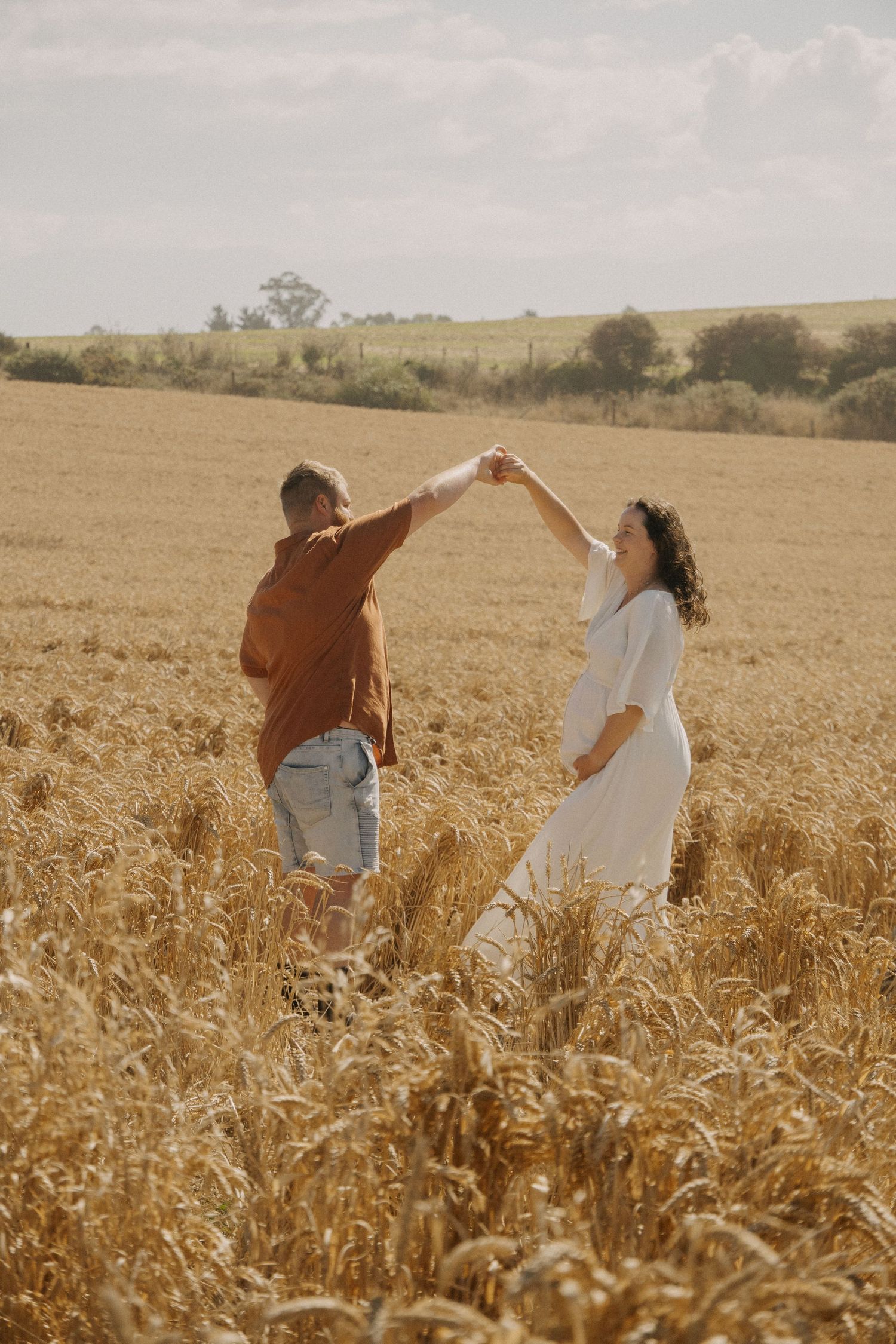 couple holding maternity bump while male spins female around