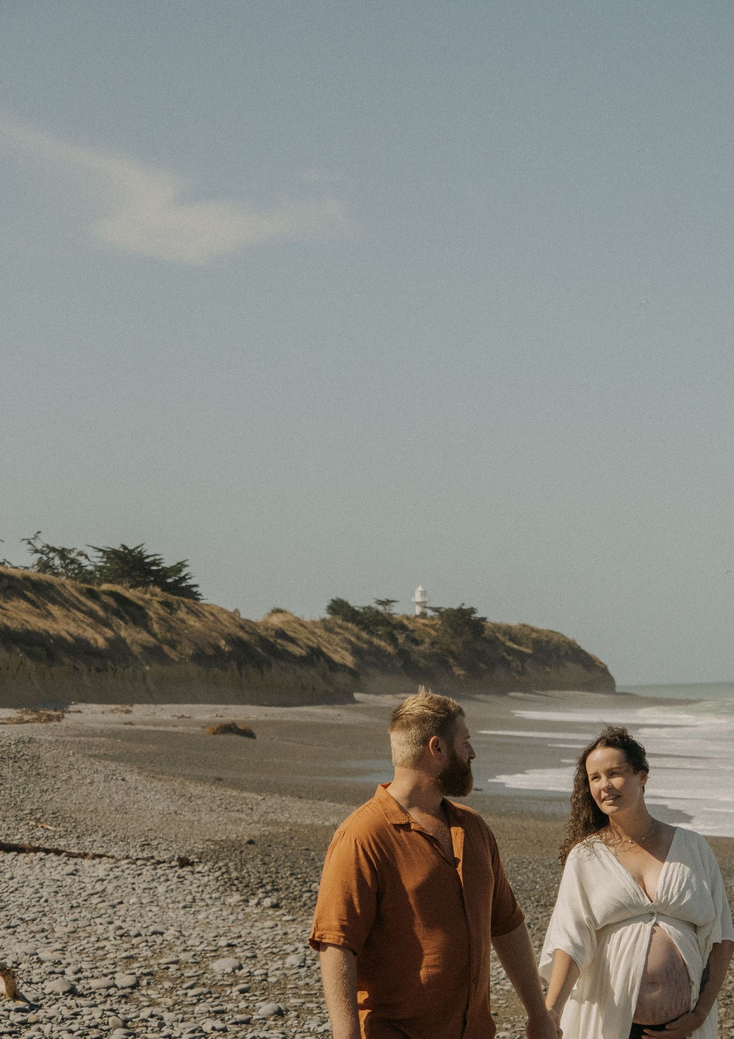 couple holding maternity bump walking along beach
