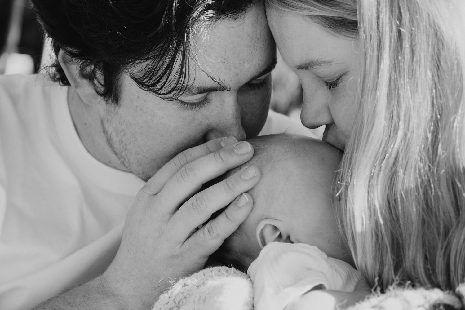 mother and father kissing newborn head