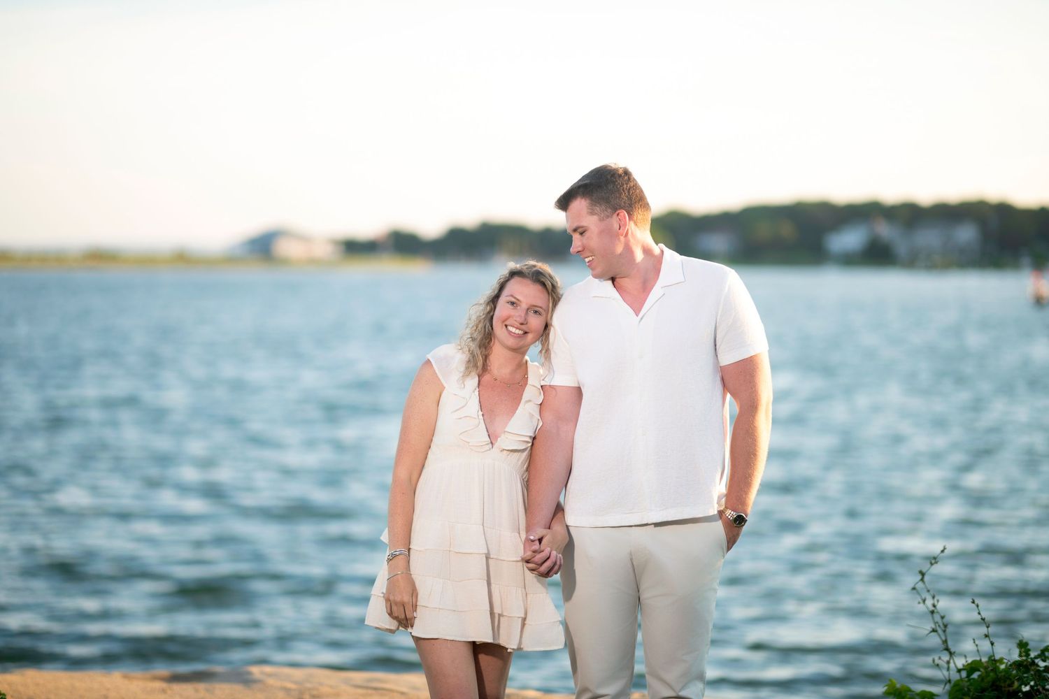 A romantic seaside photoshoot with a couple posing against the blue ocean backdrop.