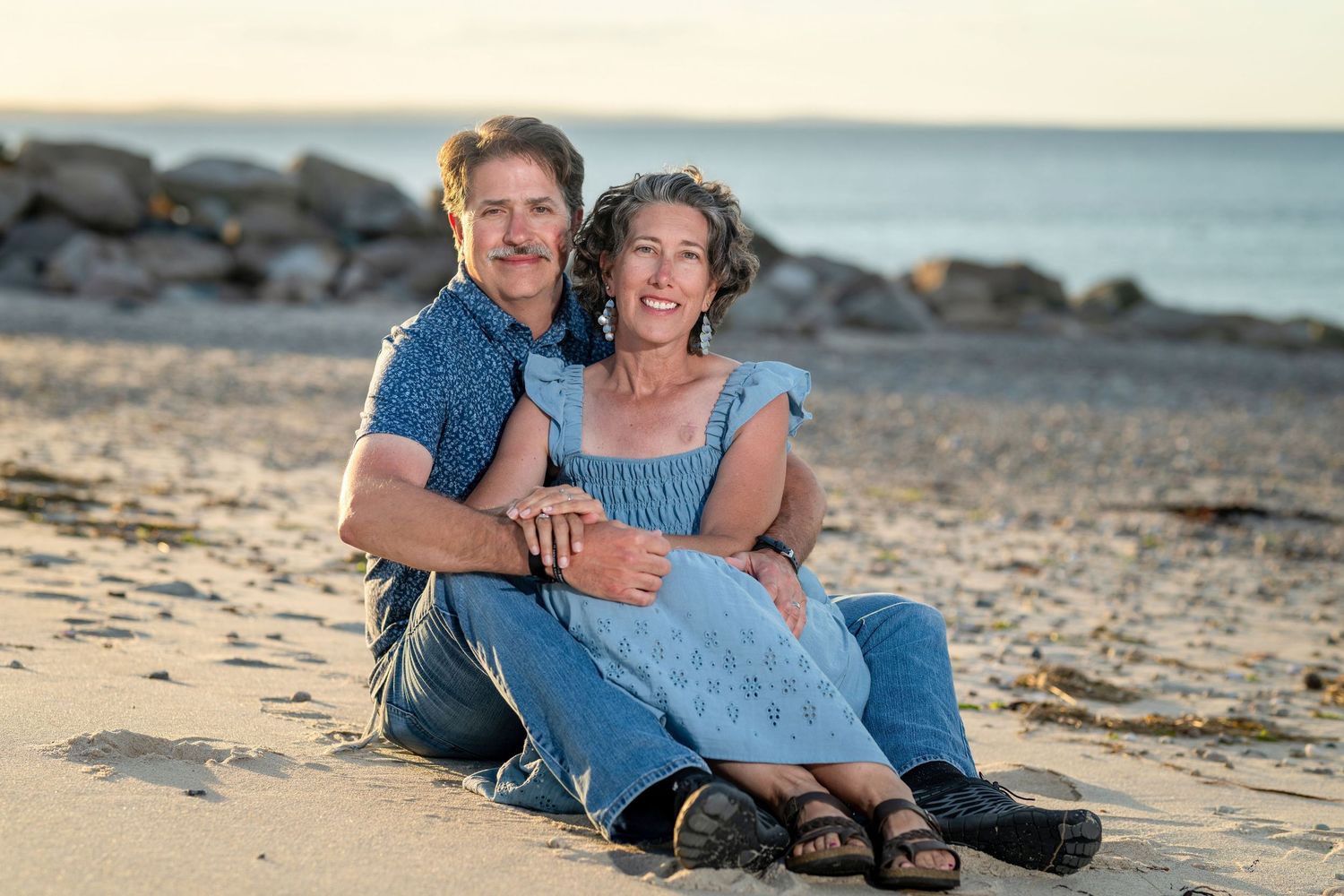 Happy couple sitting together on sandy beach, smiling warmly at camera during golden hour.