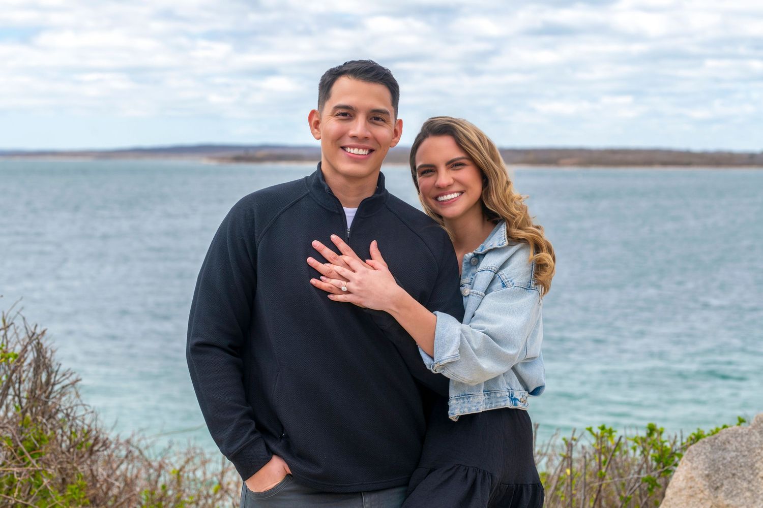 A couple poses for engagement photos along a scenic coastal area with water views.