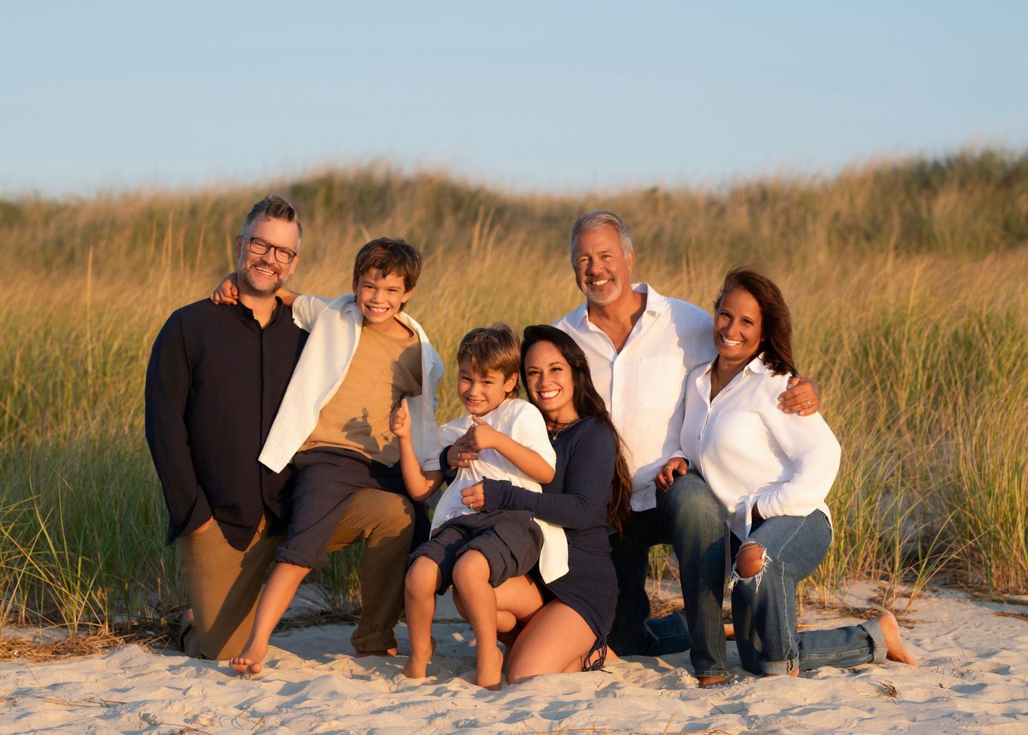 Group relaxing together on sandy beach dunes during golden hour.