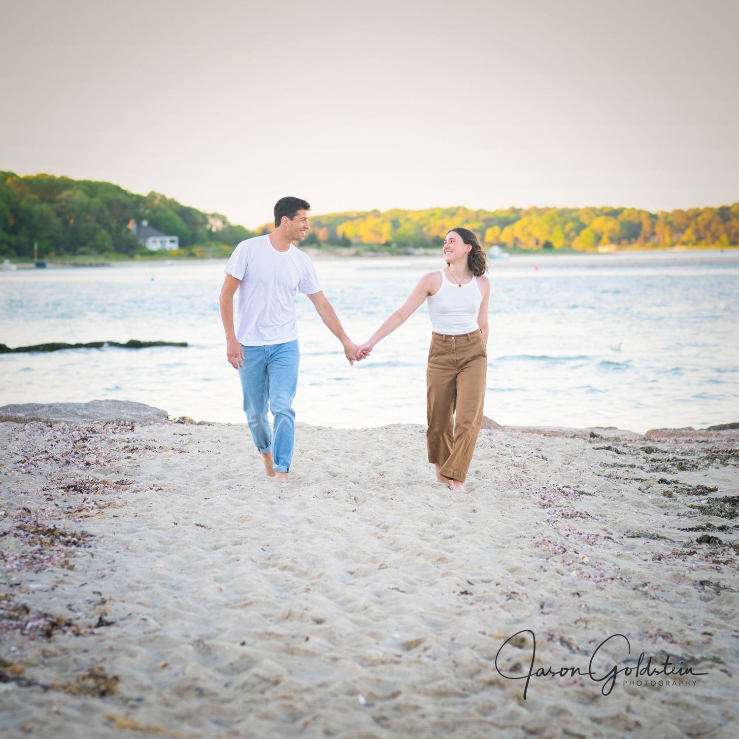 Couple walking hand in hand along a sandy beach at sunset.