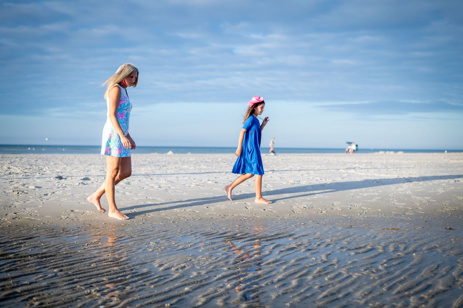 People walking along shoreline of beach during low tide.