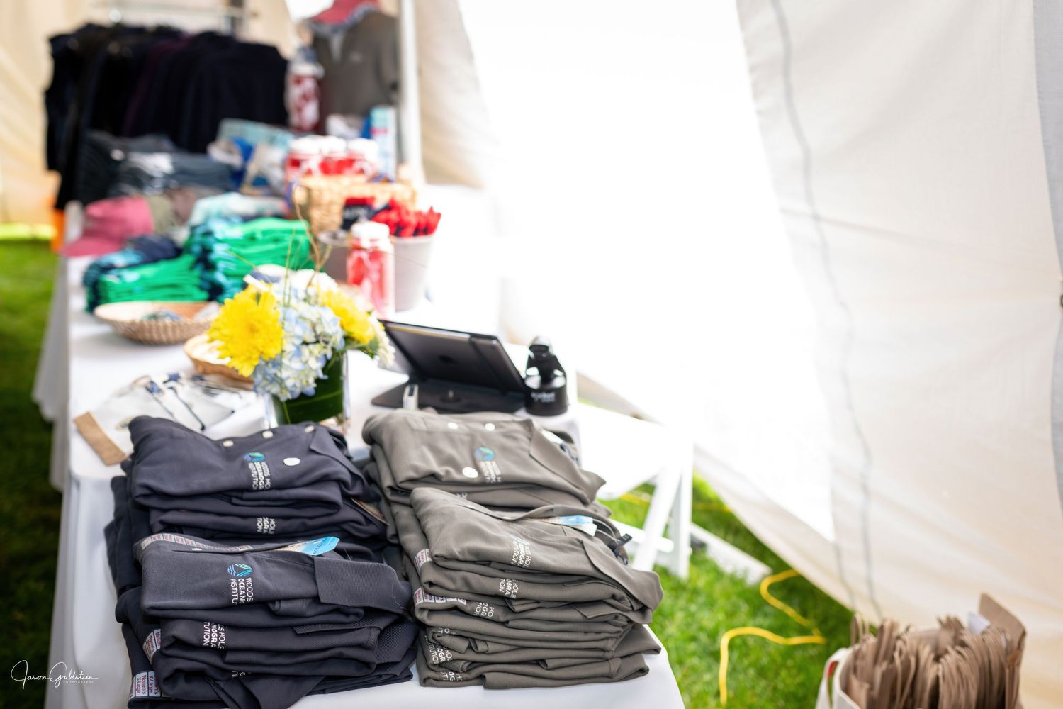 Folded clothing and merchandise displayed on tables at an event.