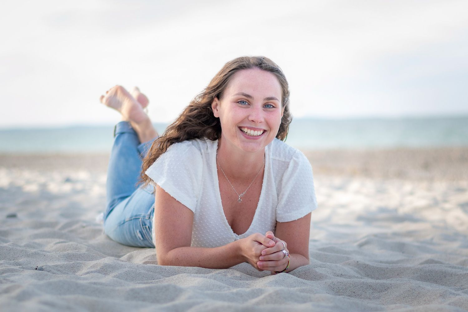 People lying on sandy beach wearing casual white clothing during outdoor photoshoot.