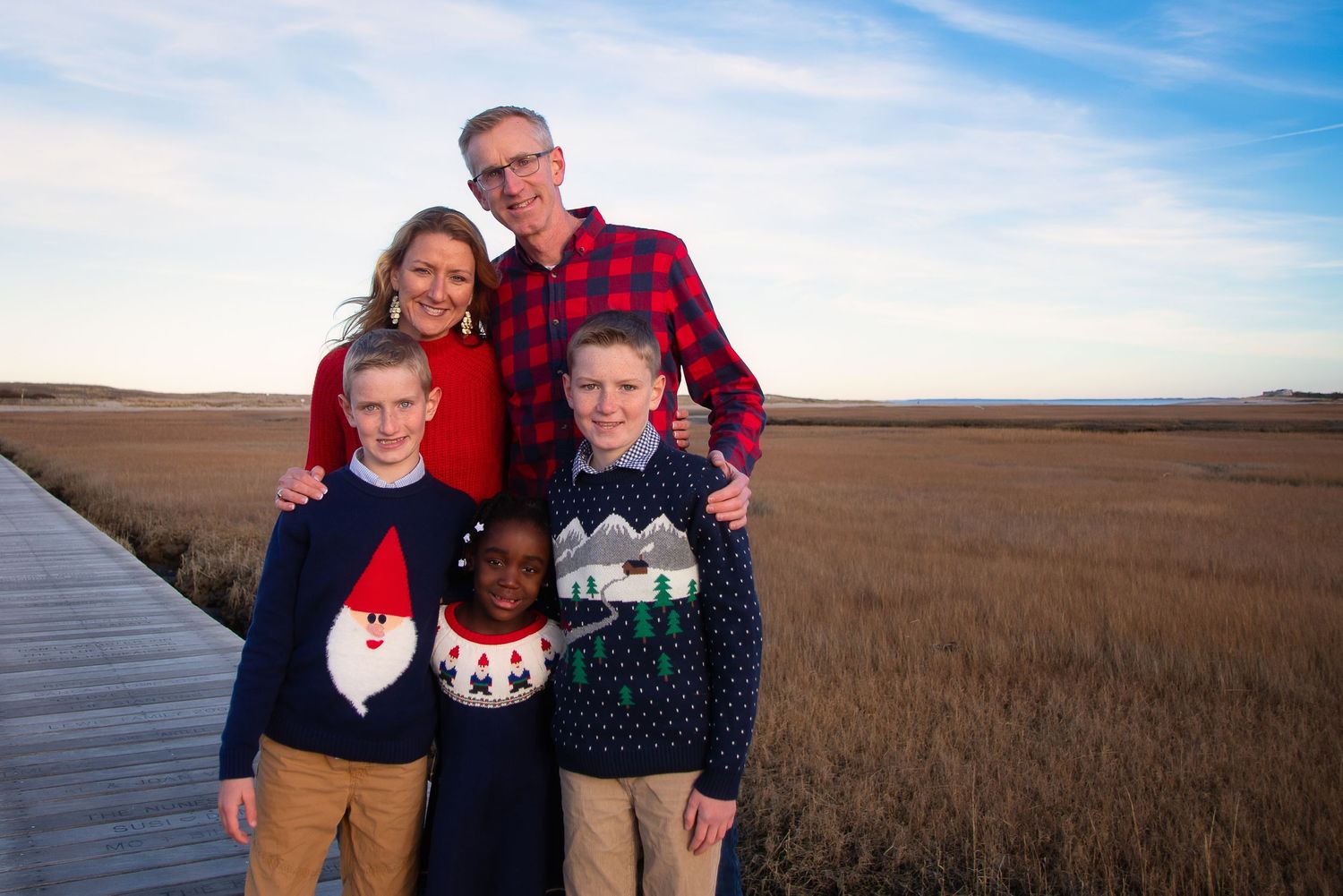 Family wearing holiday sweaters posing together in outdoor setting.