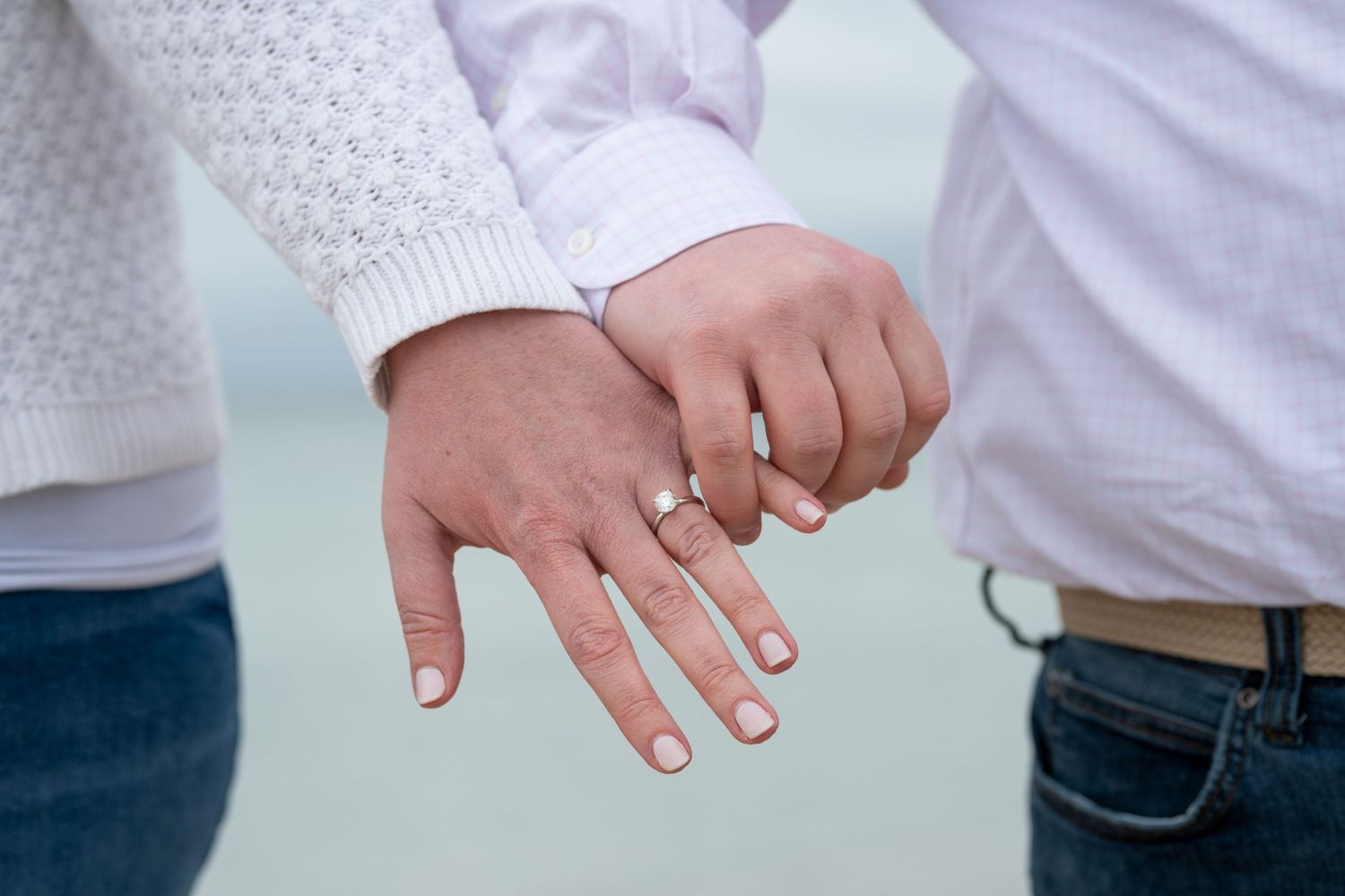 Close-up of hands showing off new engagement ring by the ocean.