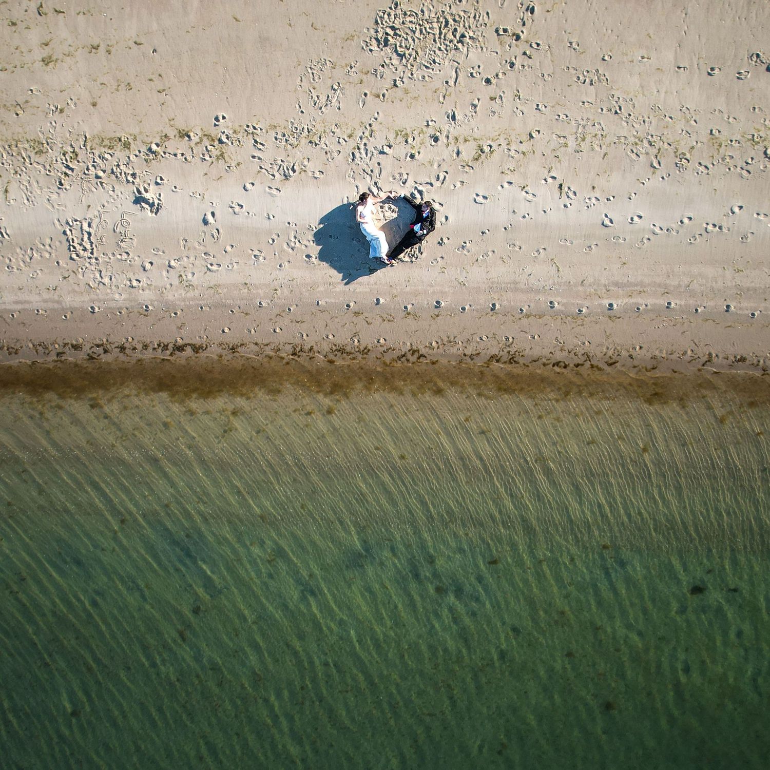 Aerial view of a sandy beach meeting turquoise water with shadows visible on shore.