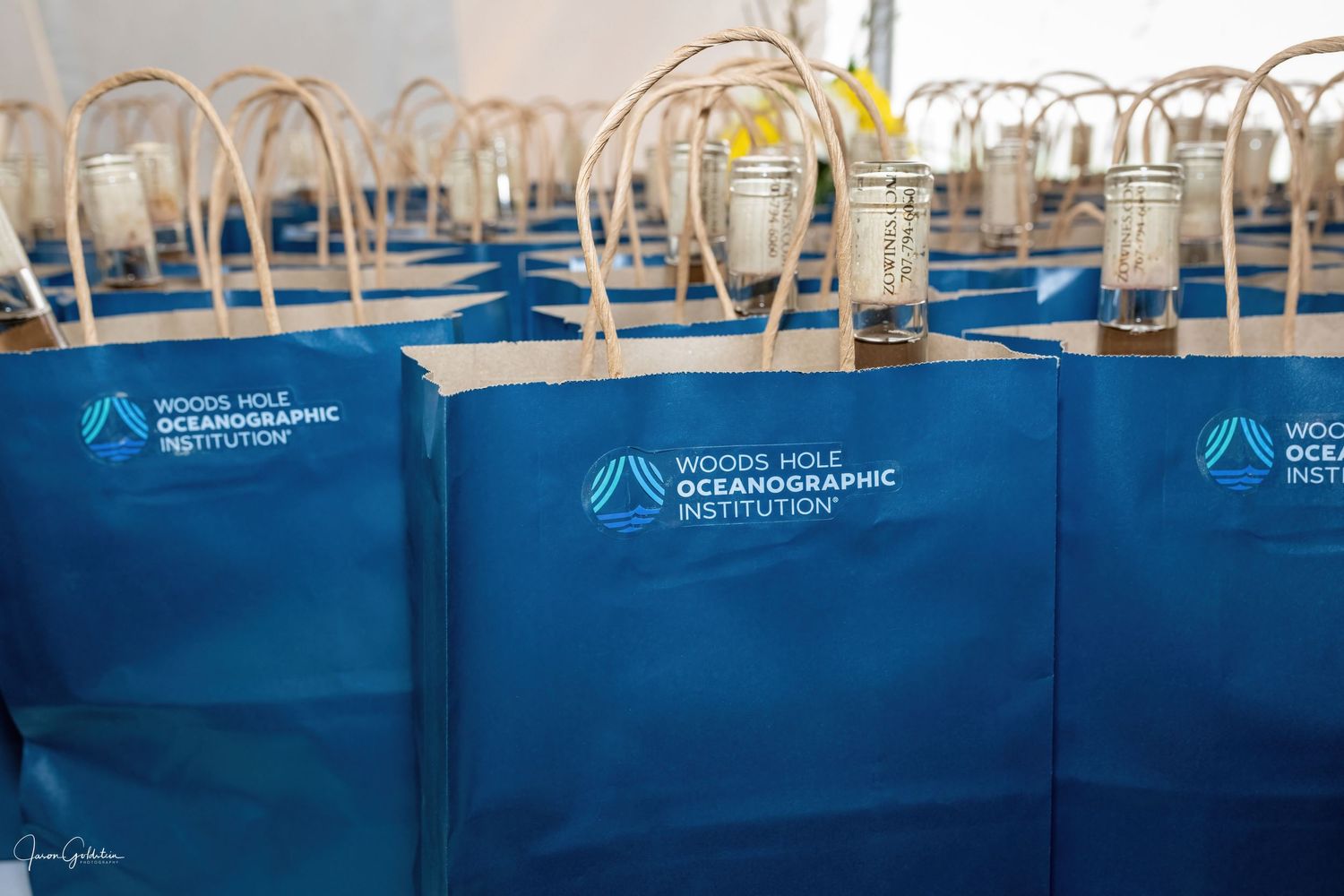 Blue branded gift bags arranged in rows on white tables at a corporate event.