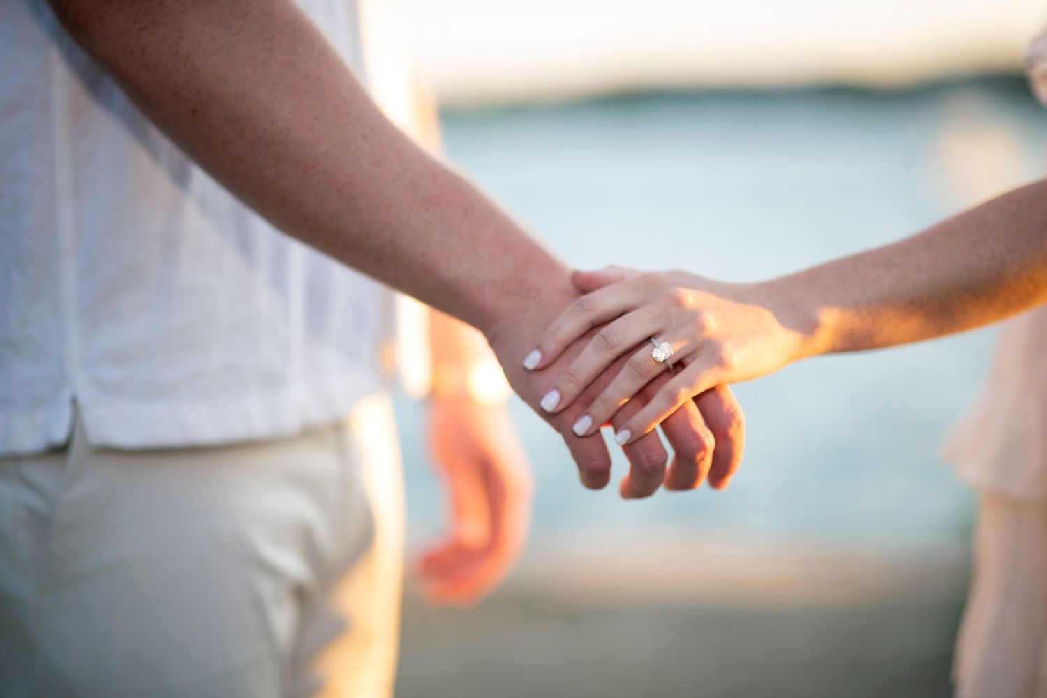 Close-up shot of hands touching during a romantic beach sunset photoshoot.