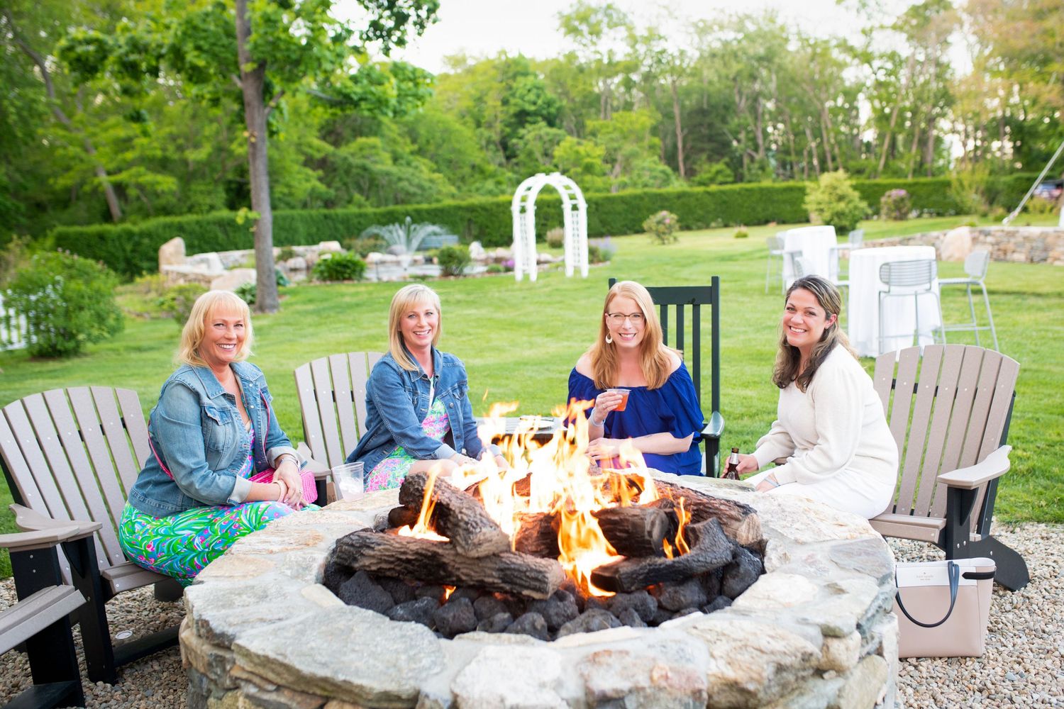 People gathered around modern stone fire pit on patio with Adirondack chairs.