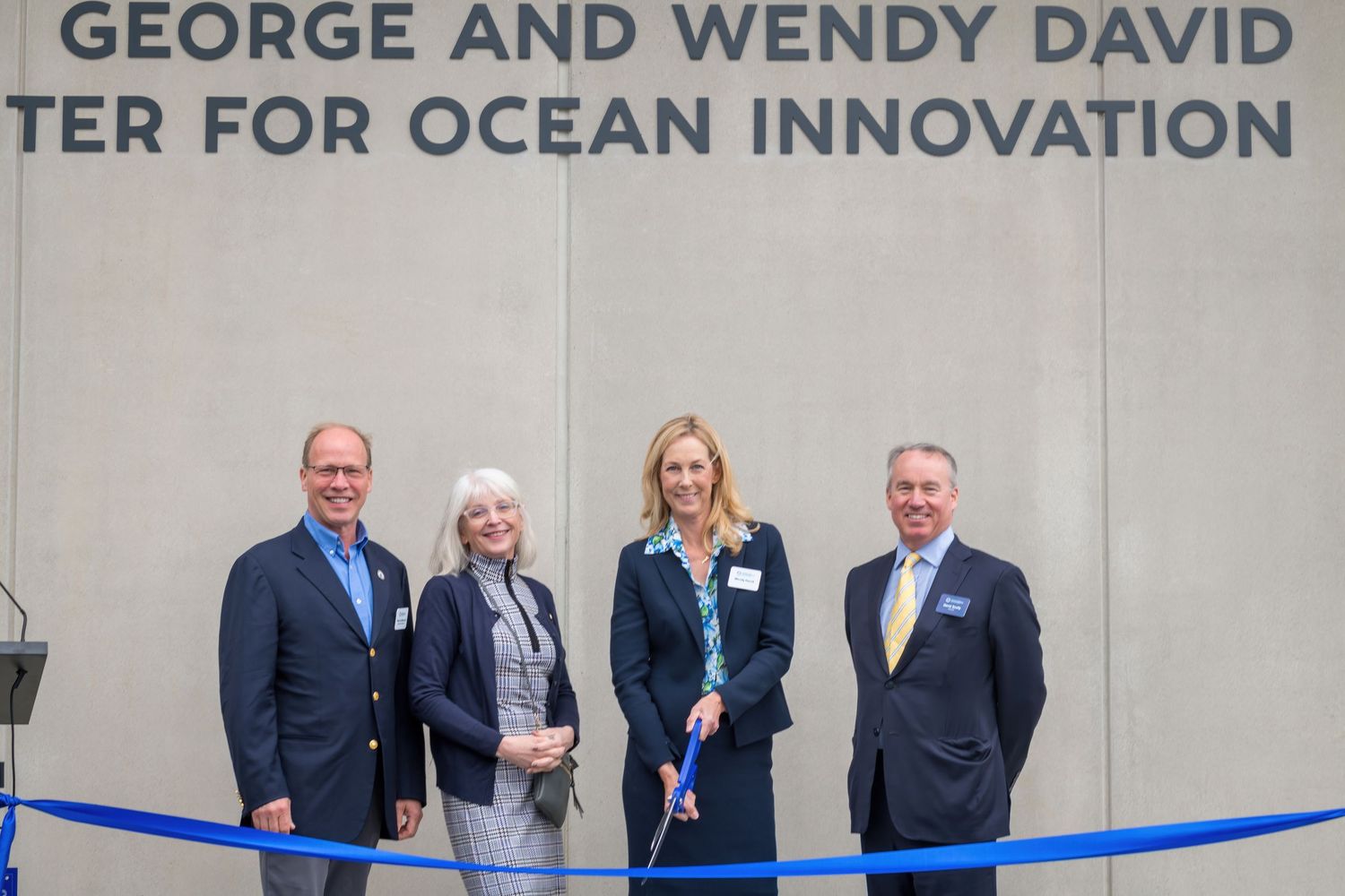 Group photo at the opening ceremony of an ocean innovation center with blue ribbon in foreground.