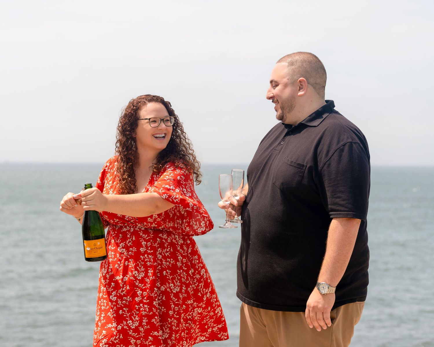 Two people sharing drinks and laughter by the ocean on a bright day.