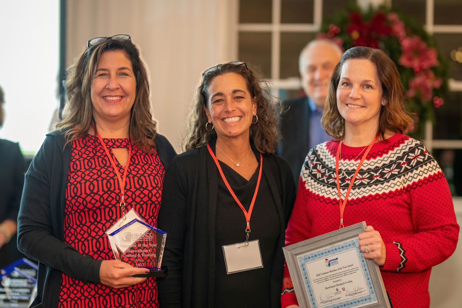 Three women in festive winter attire display awards at a holiday celebration.