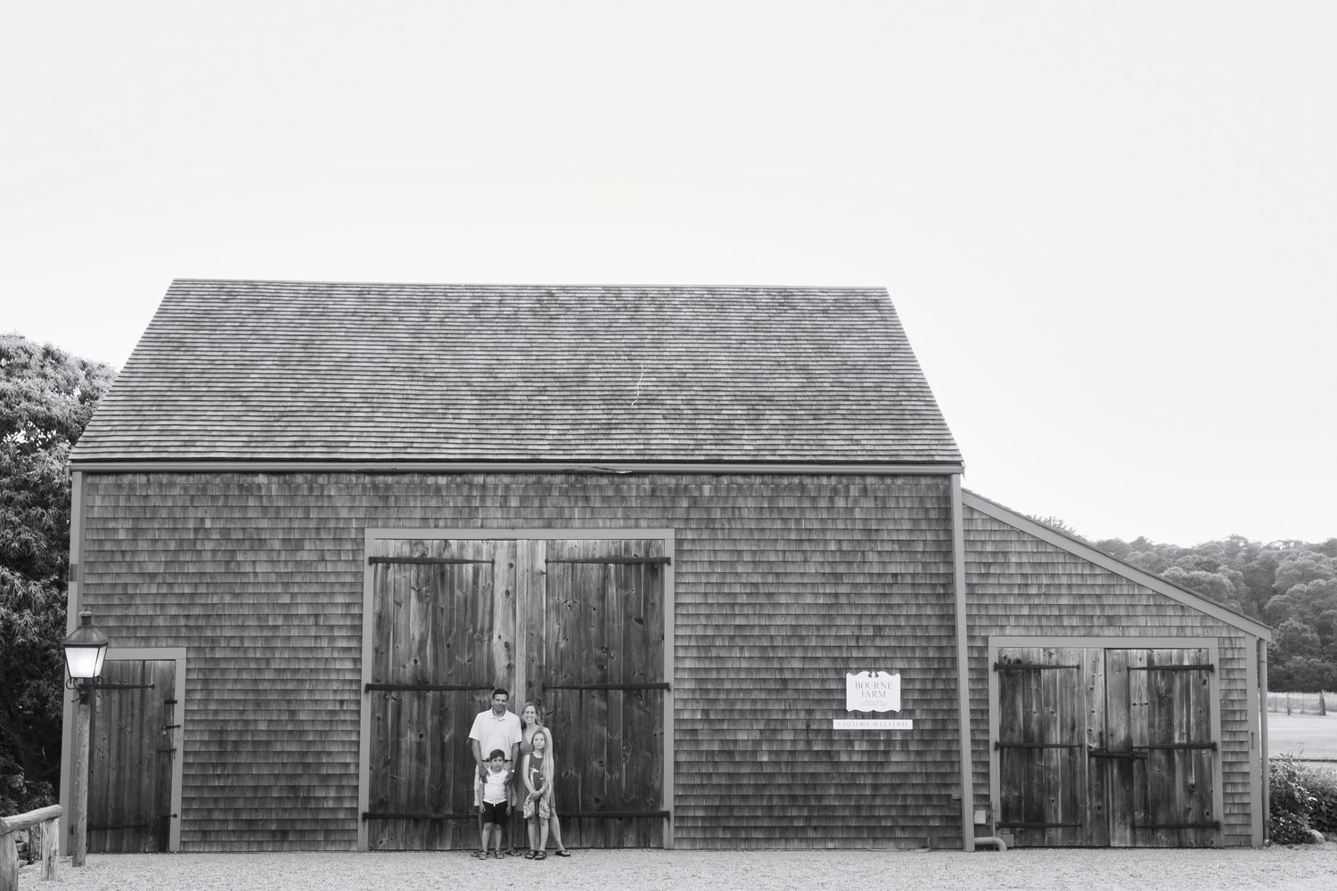 Series of weathered wooden barns with shingled siding photographed against white sky.