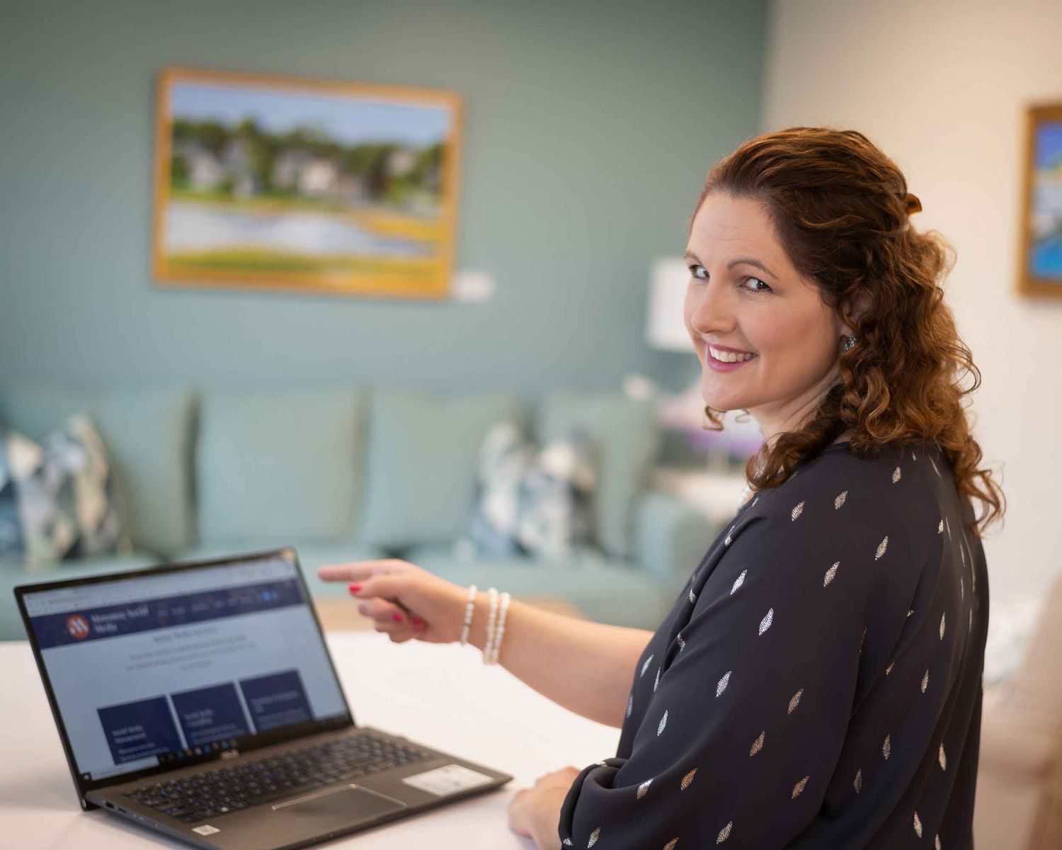 Woman smiling while pointing at a laptop screen in a modern office setting.