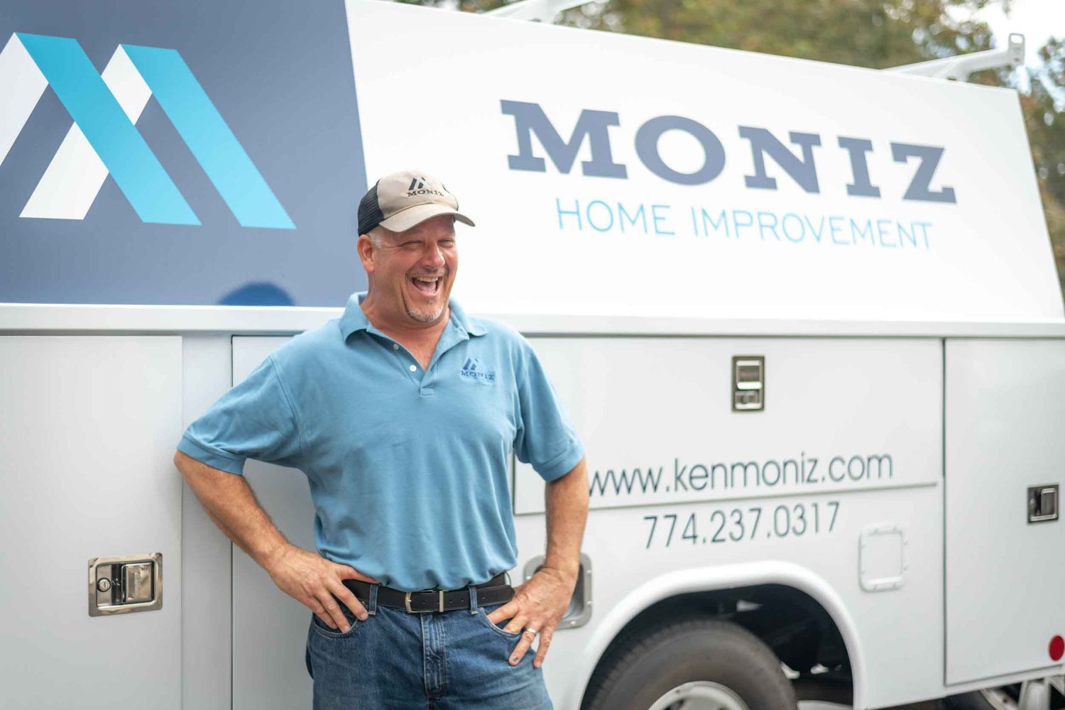 Man smiling in front of Moniz Home Improvement truck wearing blue polo shirt.