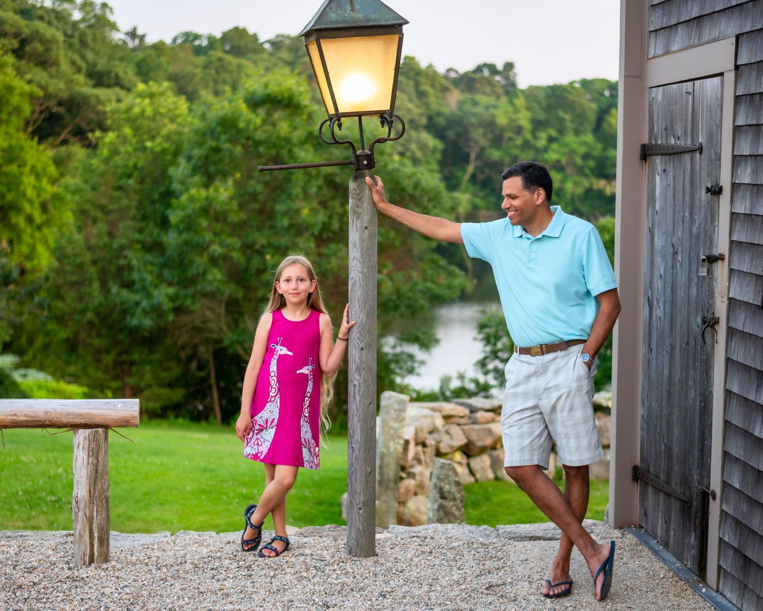 Stone pathway with vintage lamp posts leads past rustic buildings near a waterfront.
