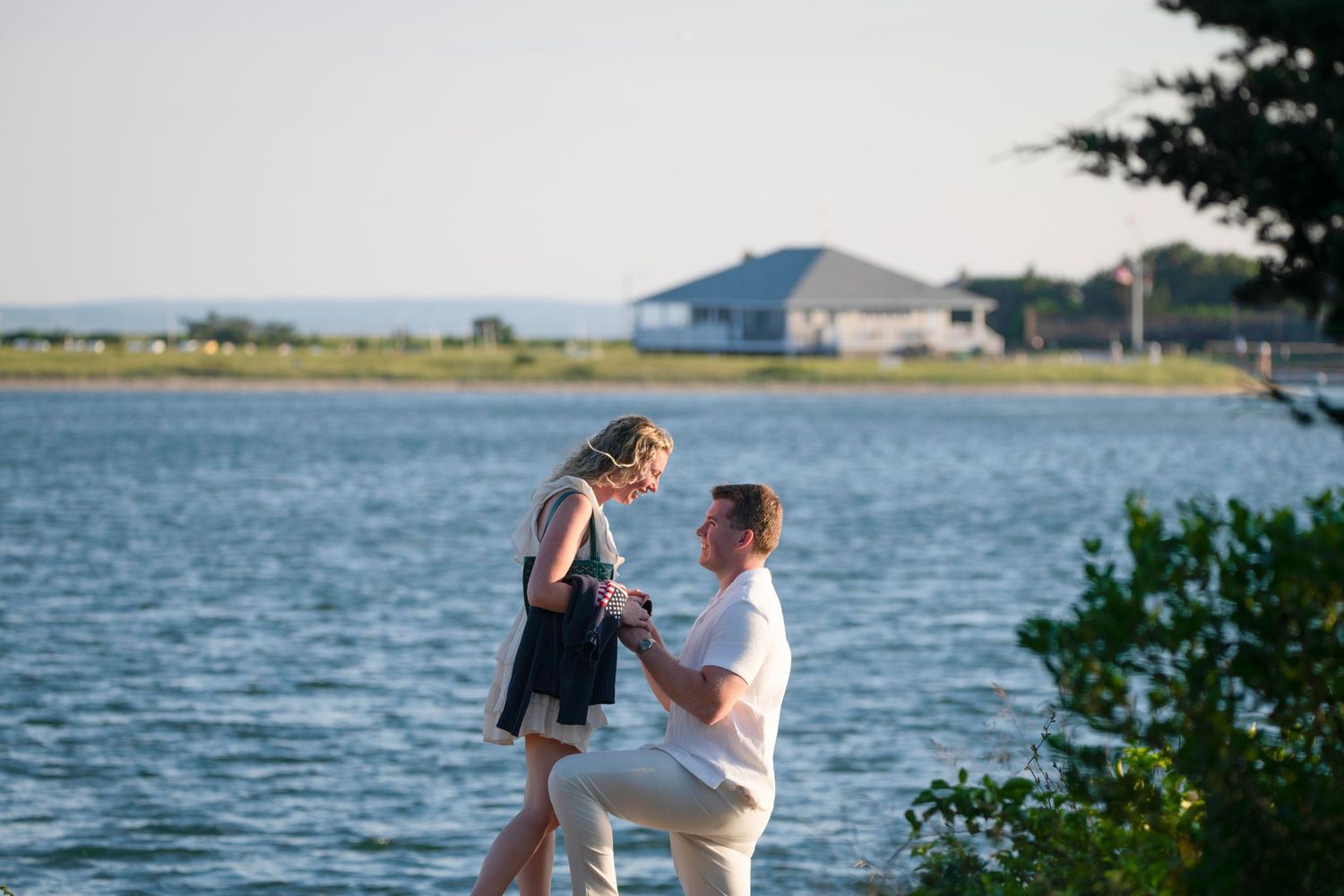 Couple sharing a romantic moment by the waterfront with coastal homes in the background.