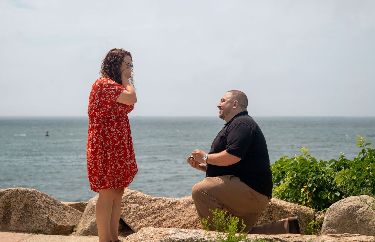 A couple poses together on rocky coastal terrain with ocean views in the background.
