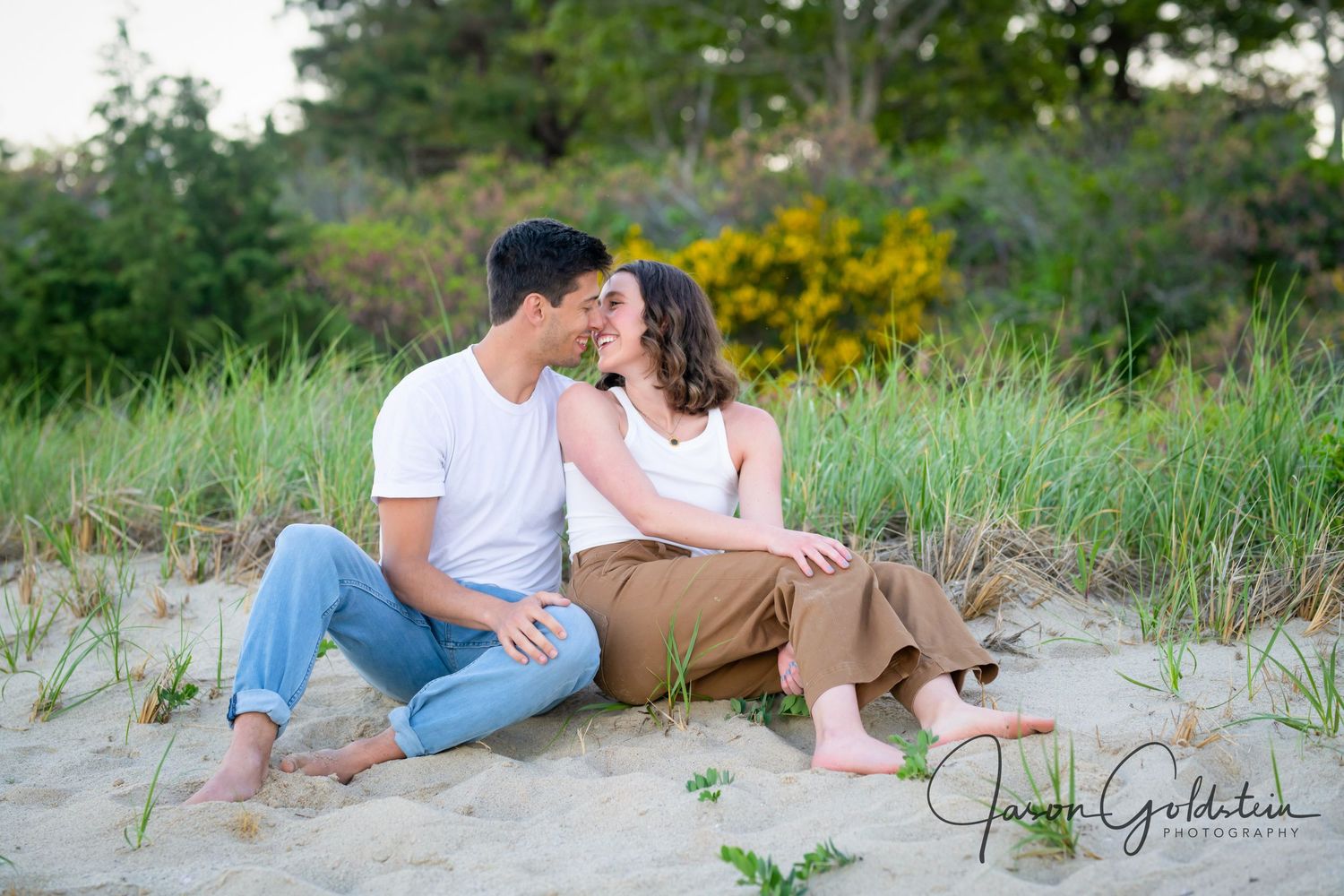 Couple relaxing on sandy dunes with beach grass and ocean views.