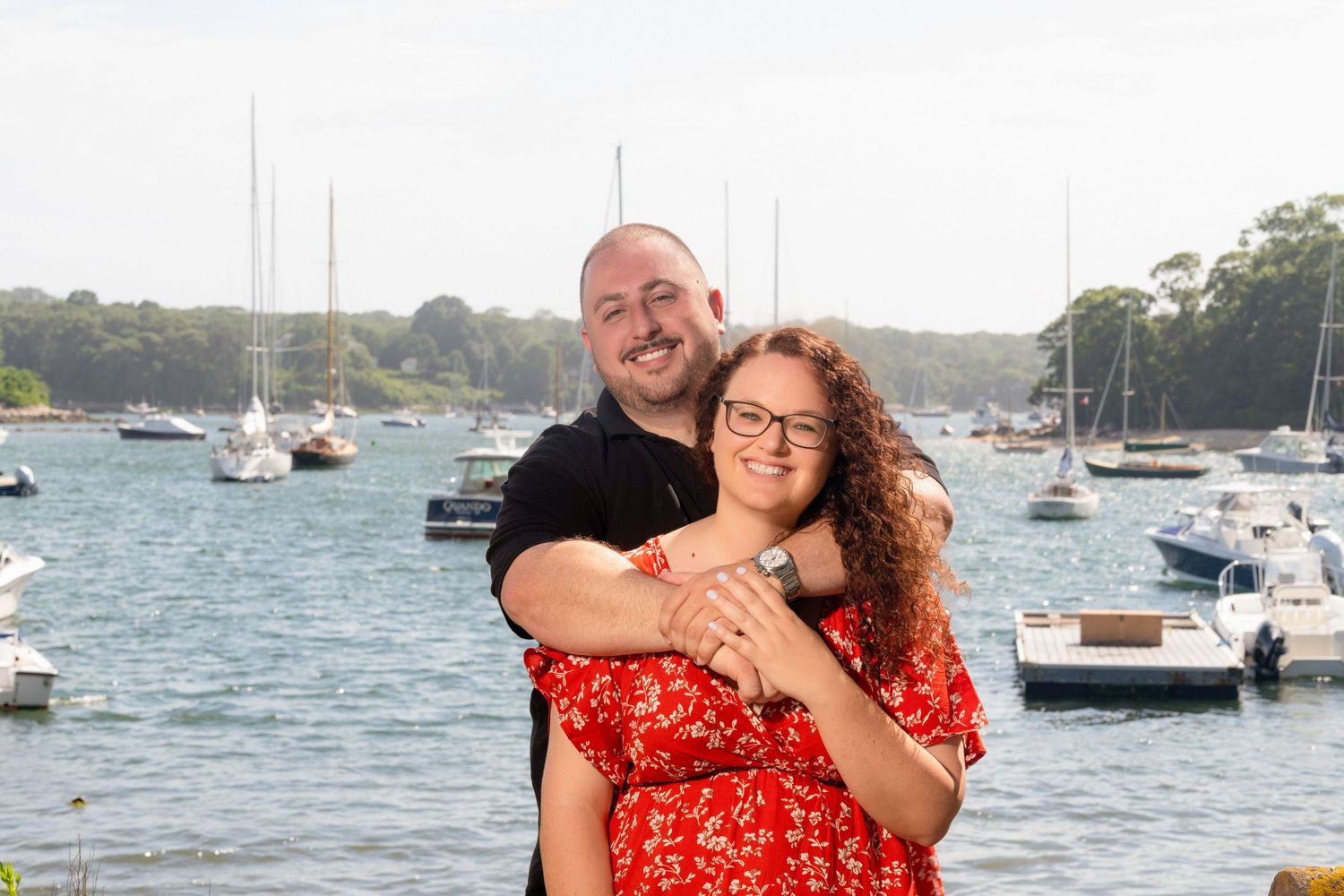 A couple enjoys a waterfront moment near boats docked in a scenic harbor.