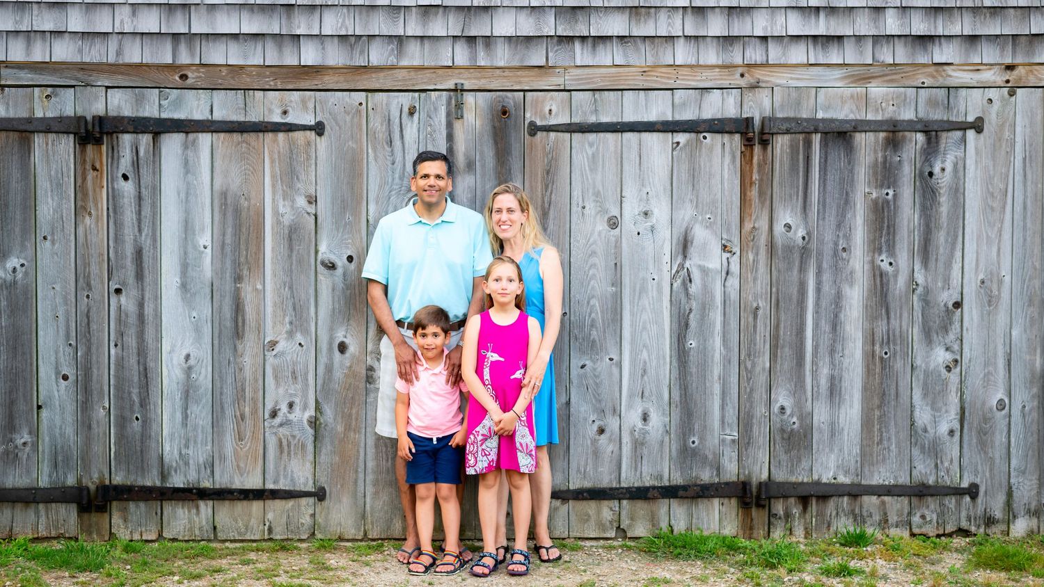 Family photo session in front of a rustic wooden barn wall.