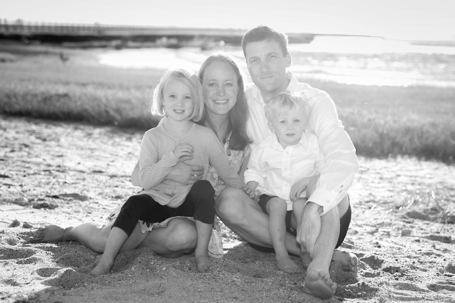 Black and white beach portrait of a family laying in the sand together.