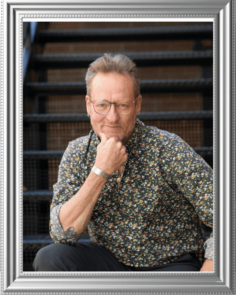 A thoughtful person in glasses and a floral print shirt sits with hand on chin against a dark background with stairs.
