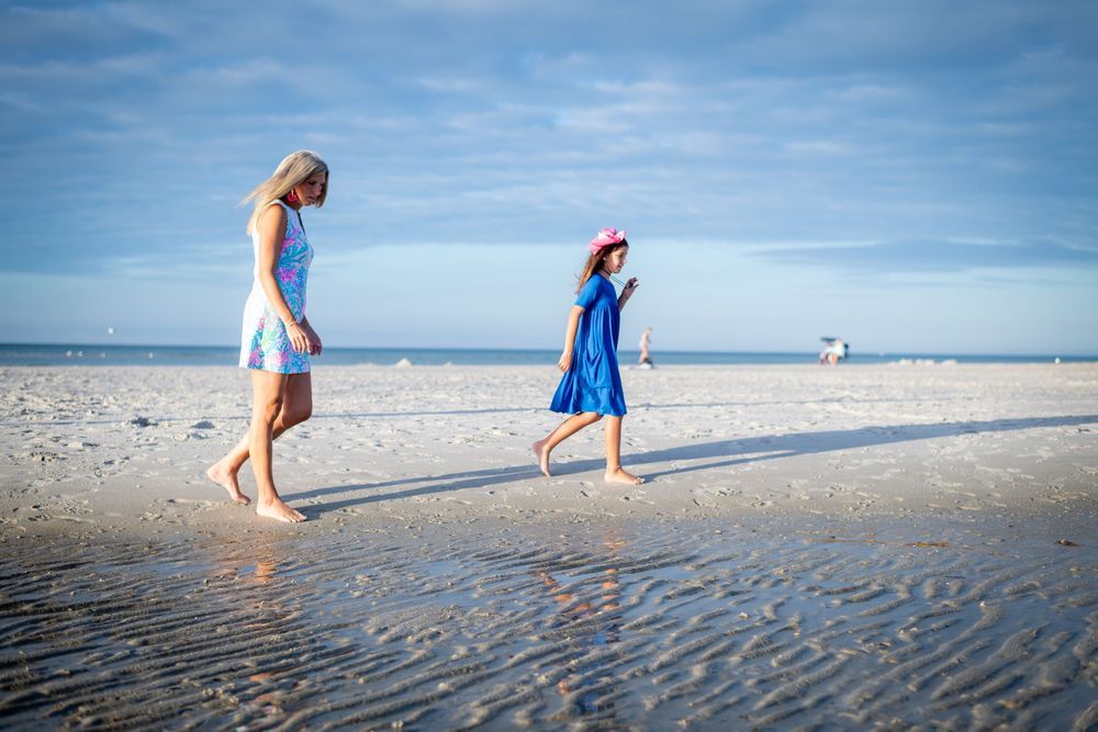 People stroll along a scenic beach with wet sand and blue ocean waves under a bright sunny sky.