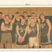 A group of athletes in sports uniforms stand together for a team photo in what appears to be a gymnasium setting.