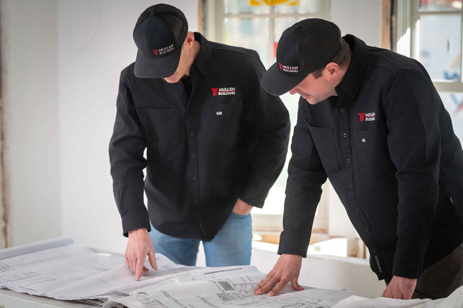 Two professionals in matching black uniforms reviewing blueprints and construction plans together.
