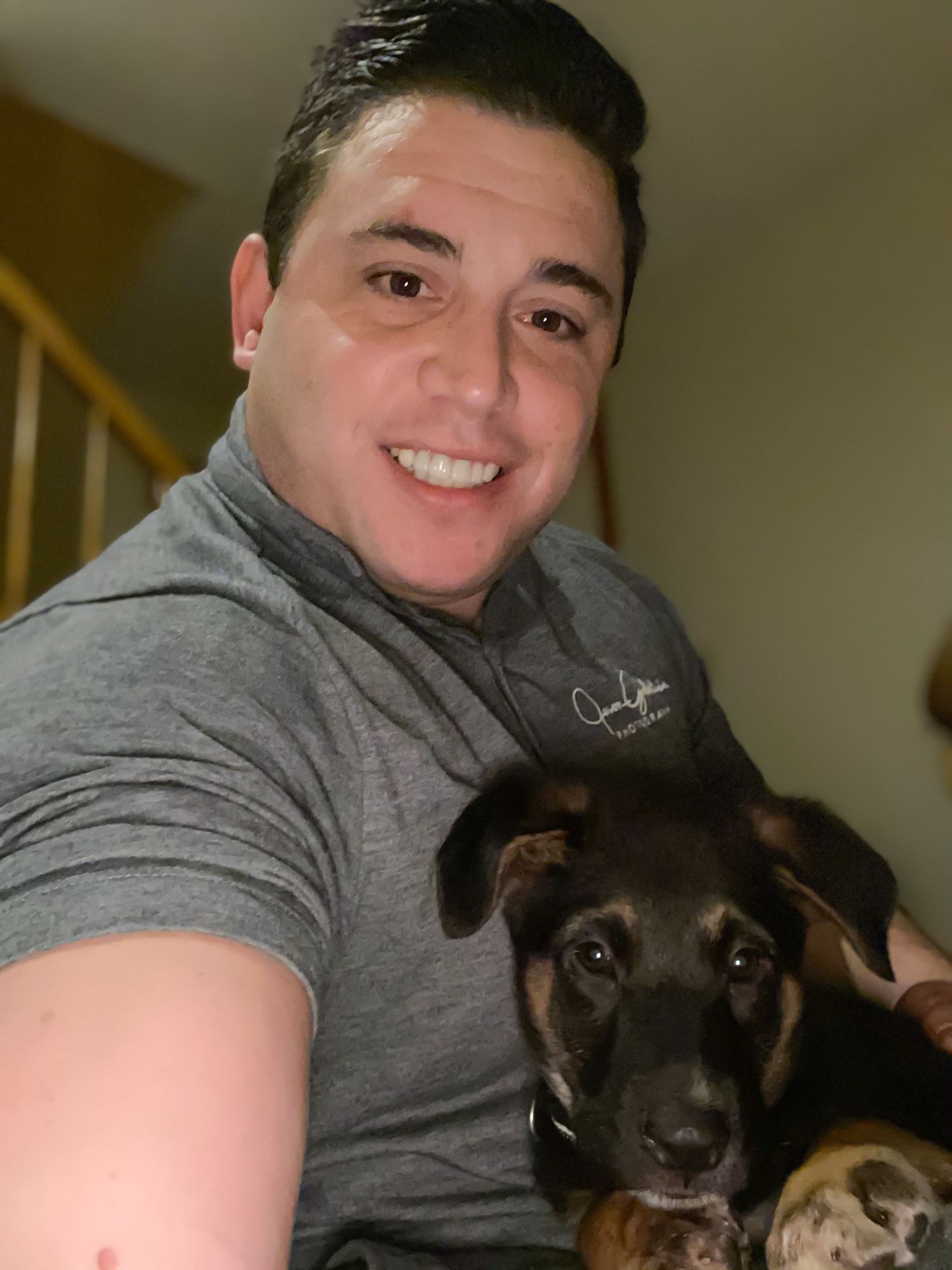 Person in grey hoodie taking selfies with two dark-colored dogs on couch indoors.