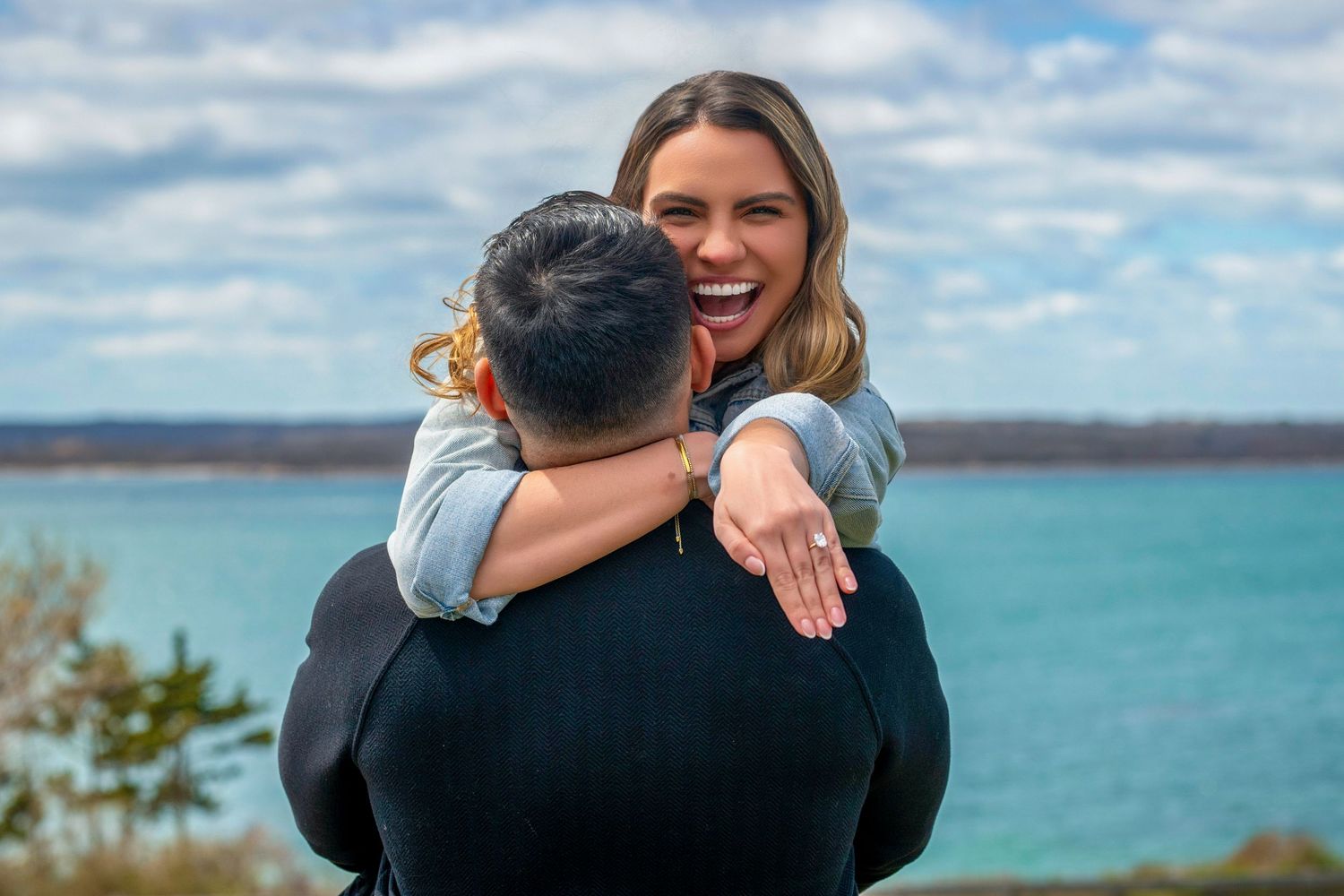 Joyful embrace captured on a scenic coastal cliff with turquoise waters in the background.