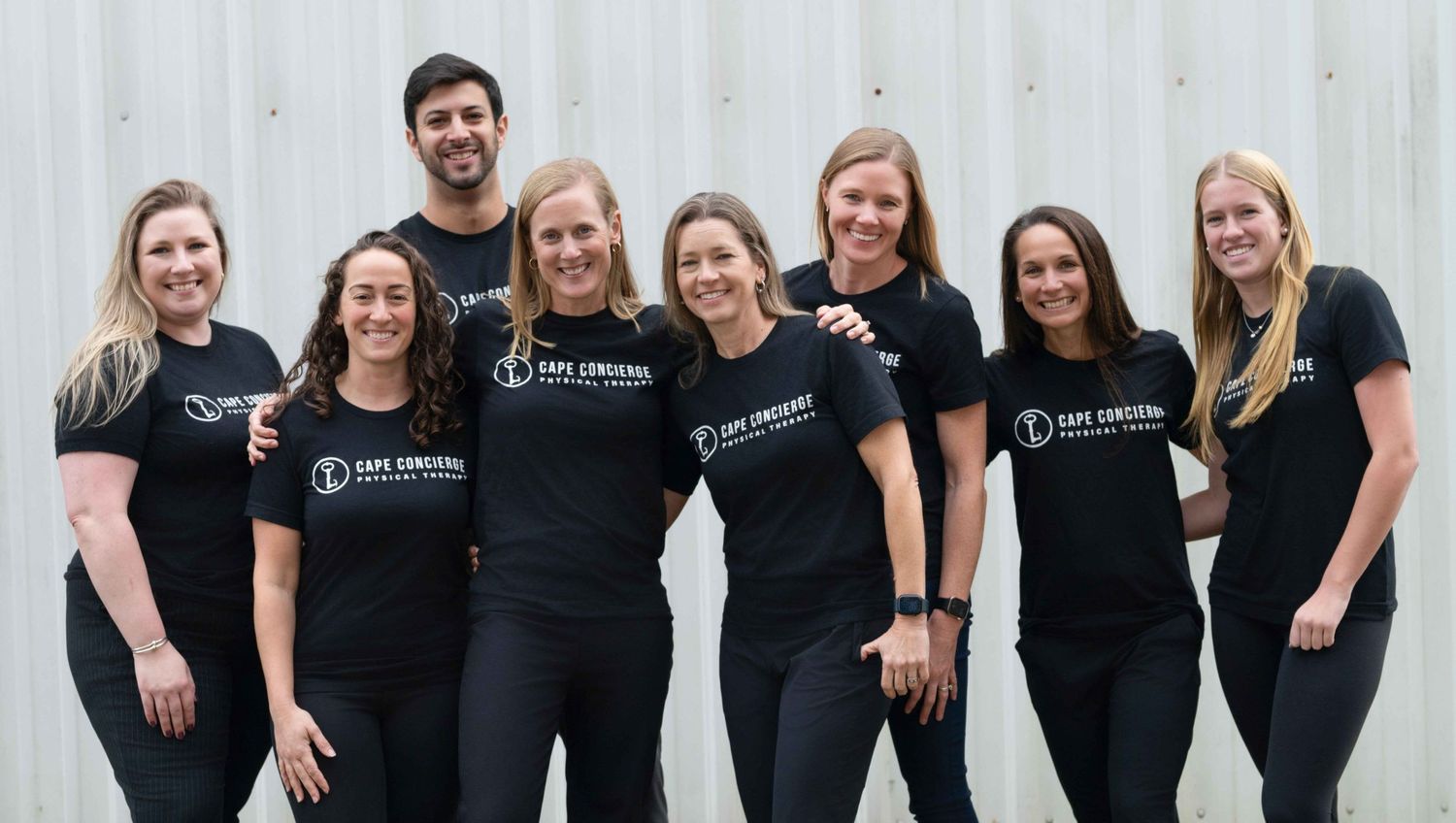 Group of eight fitness professionals in matching black Core Coaching branded t-shirts posing together outdoors.