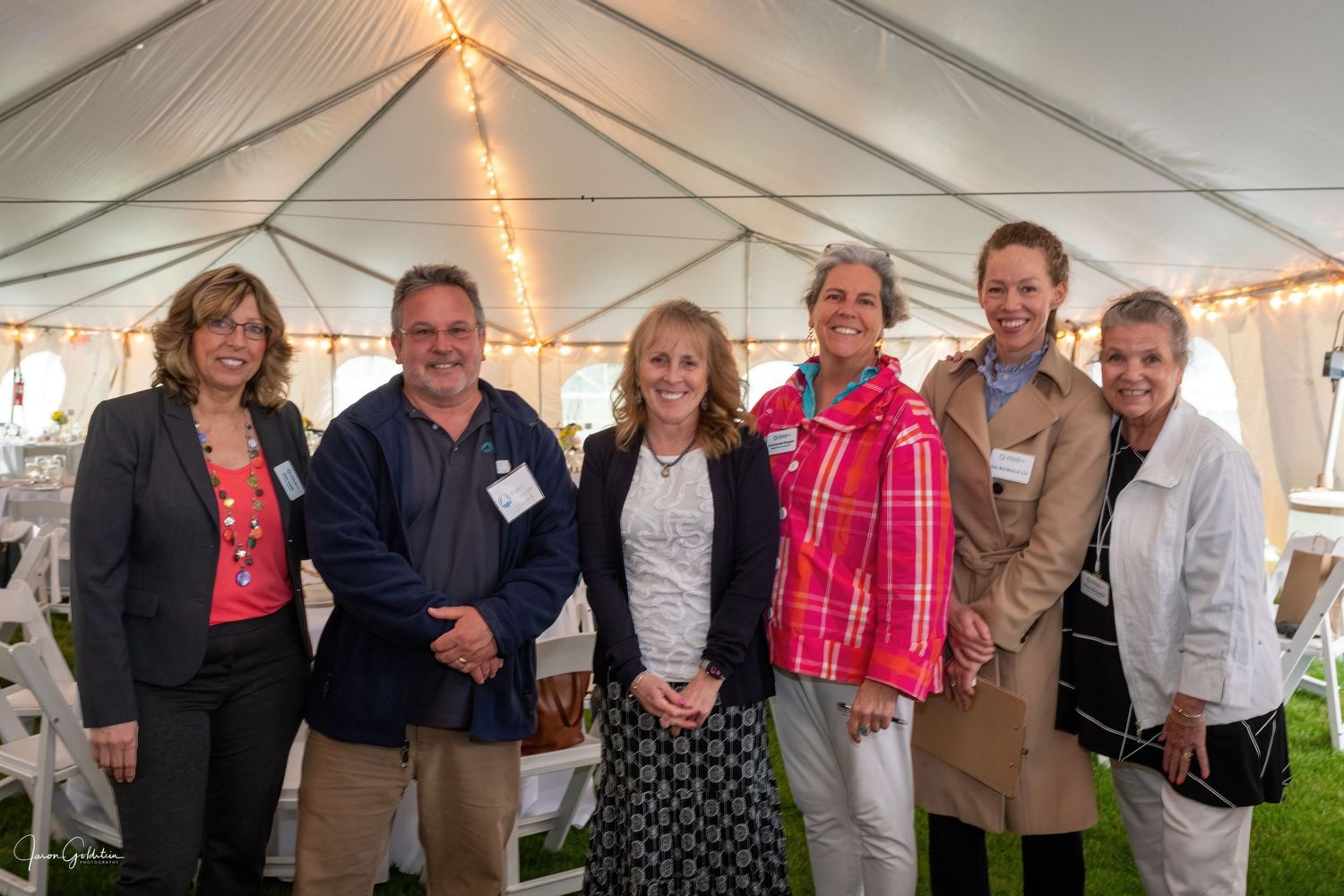 Group of attendees gathered under an outdoor event tent during an evening celebration.