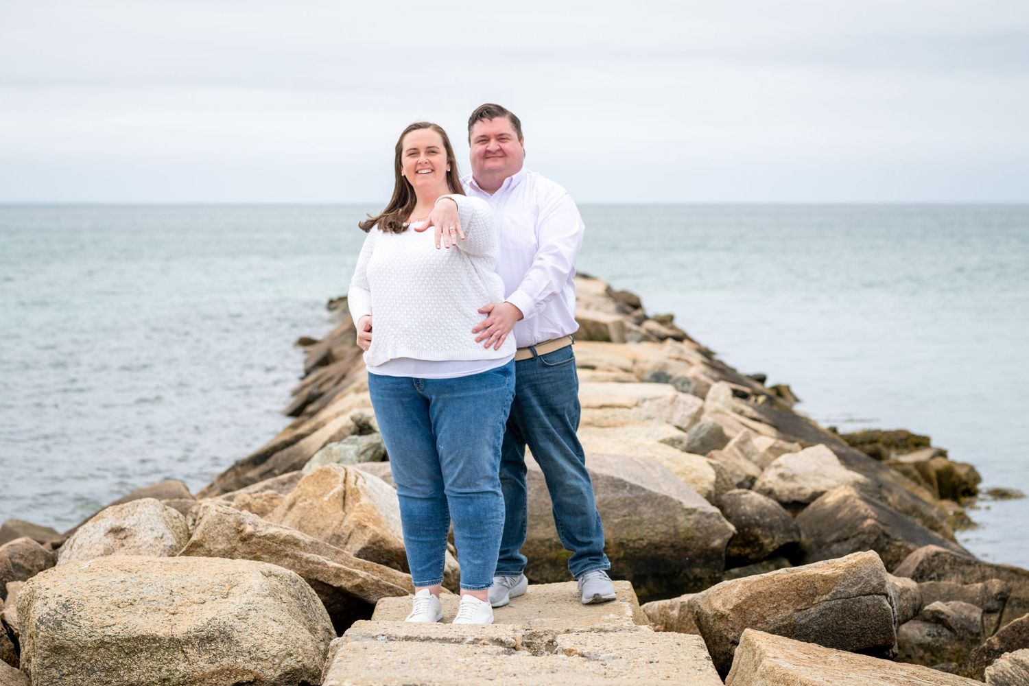 Newly engaged couple standing on rocky coastal outcrop with ocean views.
