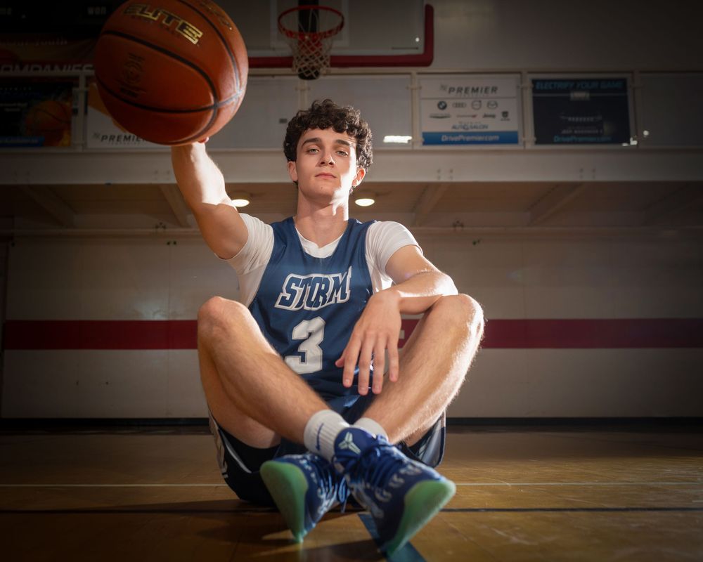 Young basketball player in Storm jersey #3 sits on gym floor spinning ball on finger.