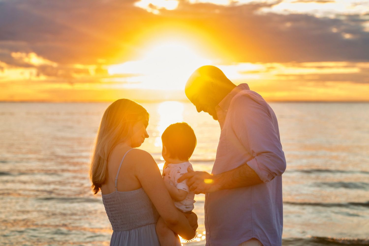 Silhouettes of a couple embrace on a beach during a vibrant orange sunset over the ocean.